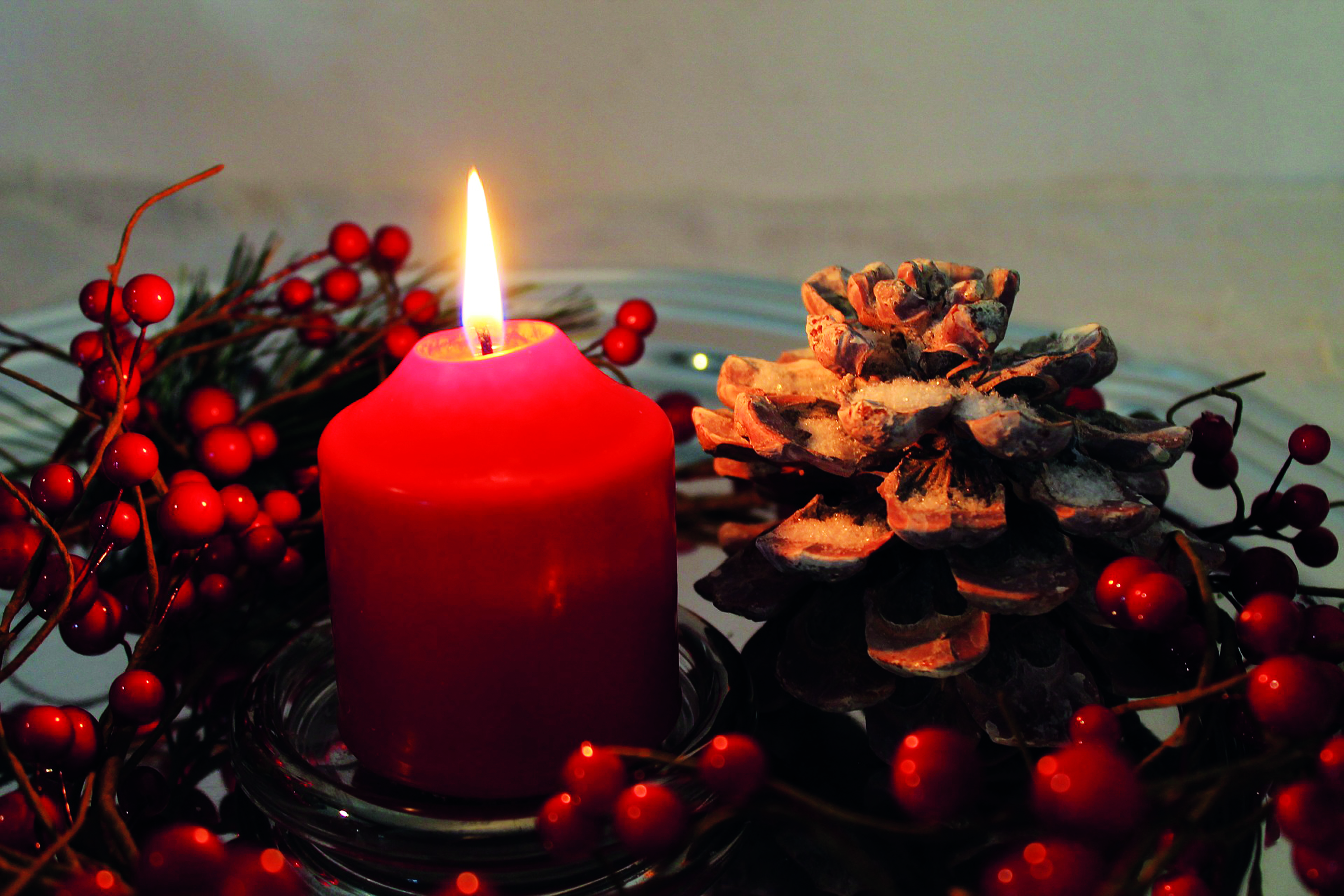 Weihnachtliches Bild: brennende rote Kerze mit roten Beeren und Tannenzapfen