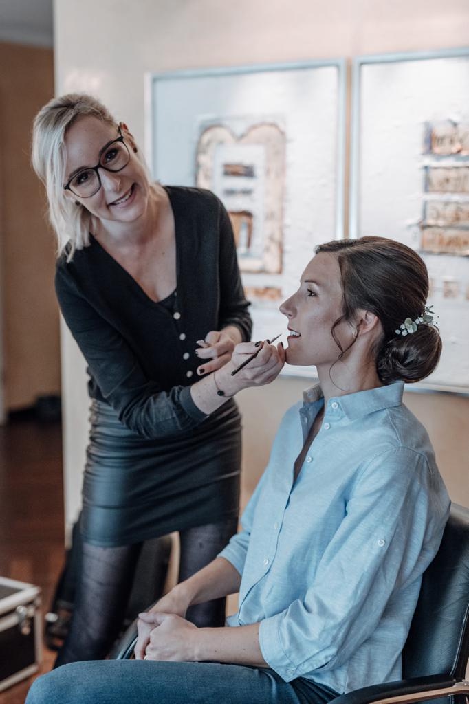 Hair & Make-up Stylistin beim Schminken der Braut