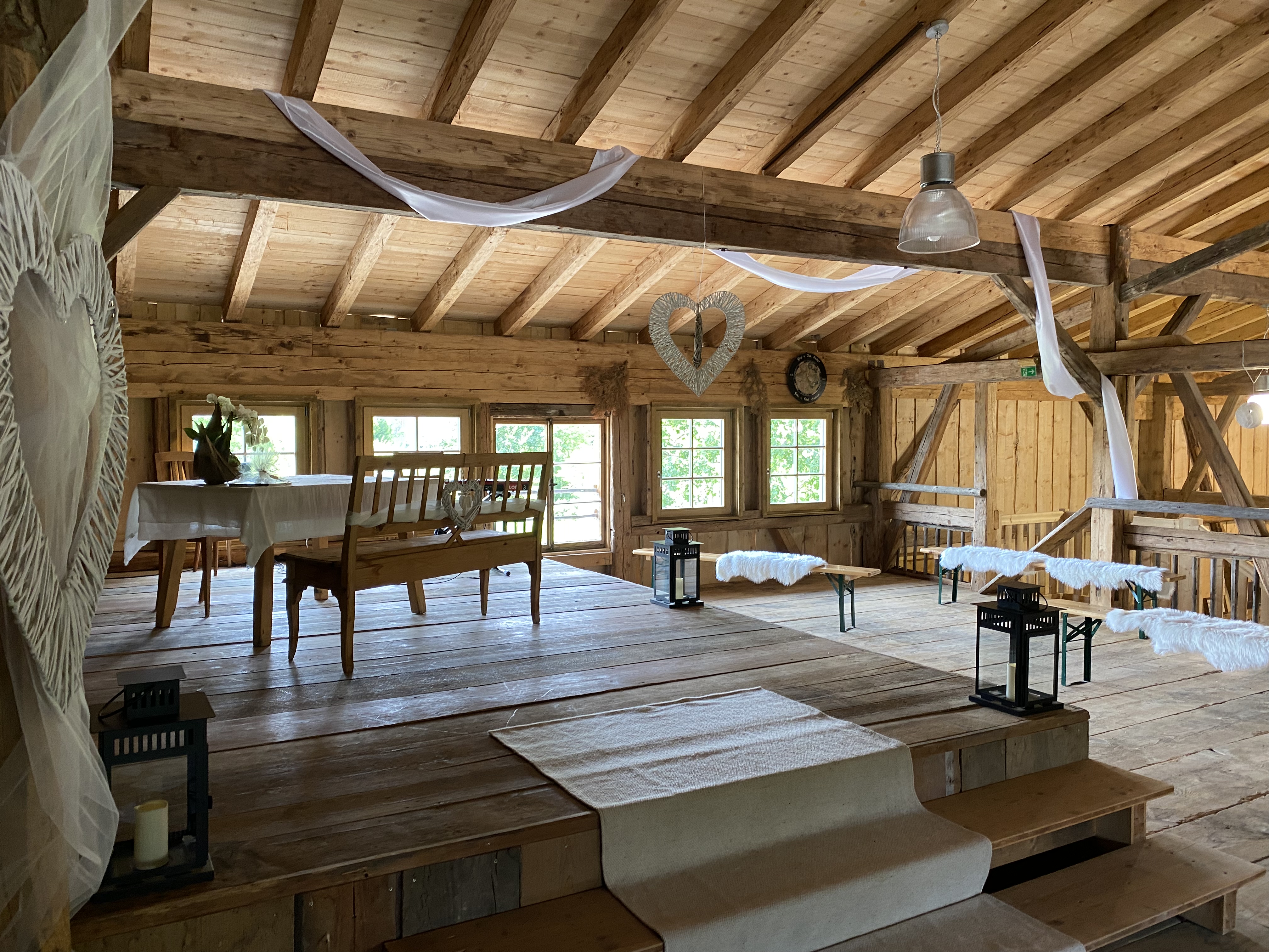 Dekorierter Innenraum der Tenne aus Holz in Ofterschwang. Trautisch mit Tischdecke, Bänke mit Fell. Viele Fenster.