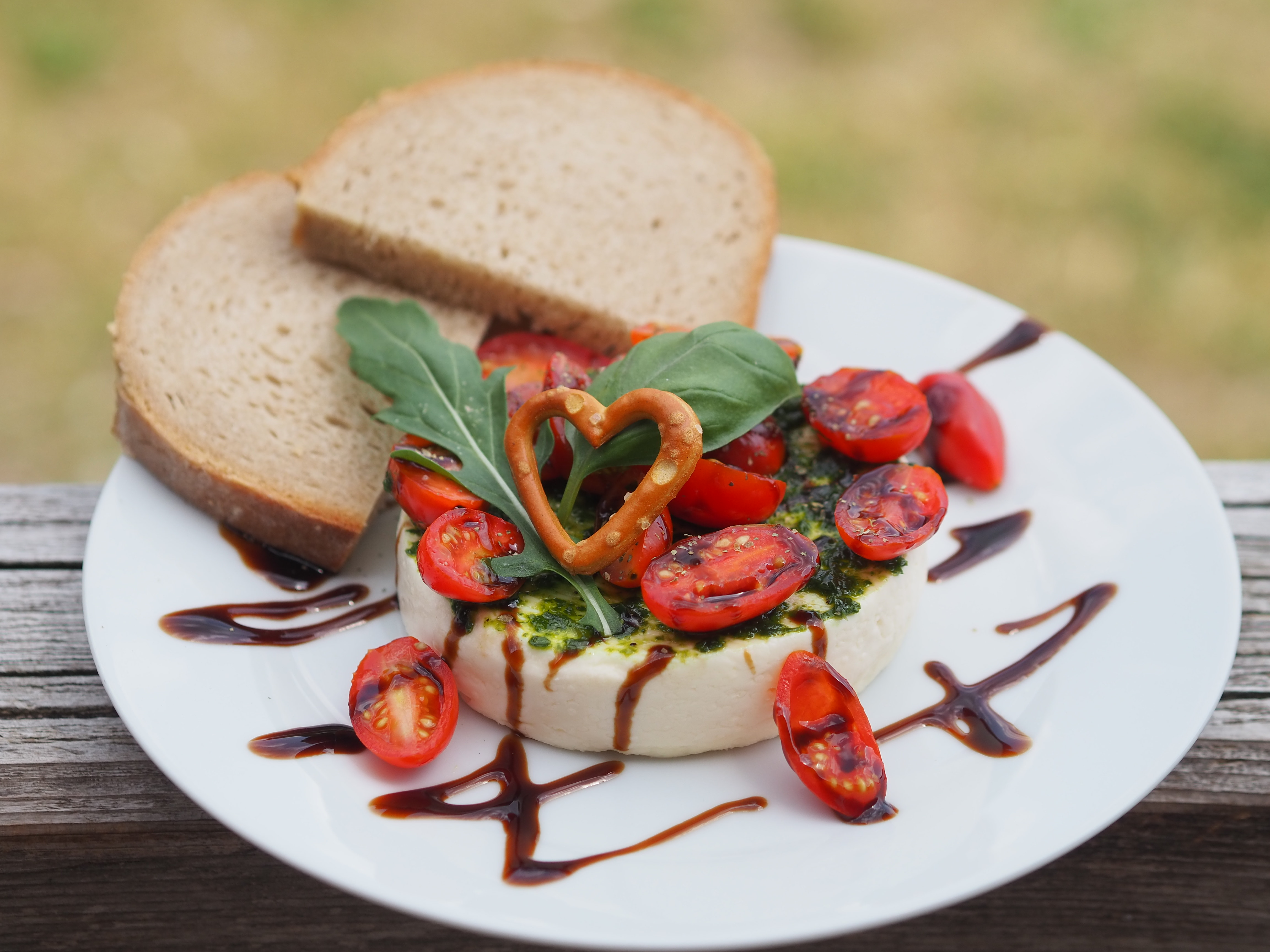Auf Teller angerichteter Weichkäse mit Tomaten, Pesto und Brotscheiben - Ein Rezept einer Alpe in den Hörnerdörfern im Allgäu 