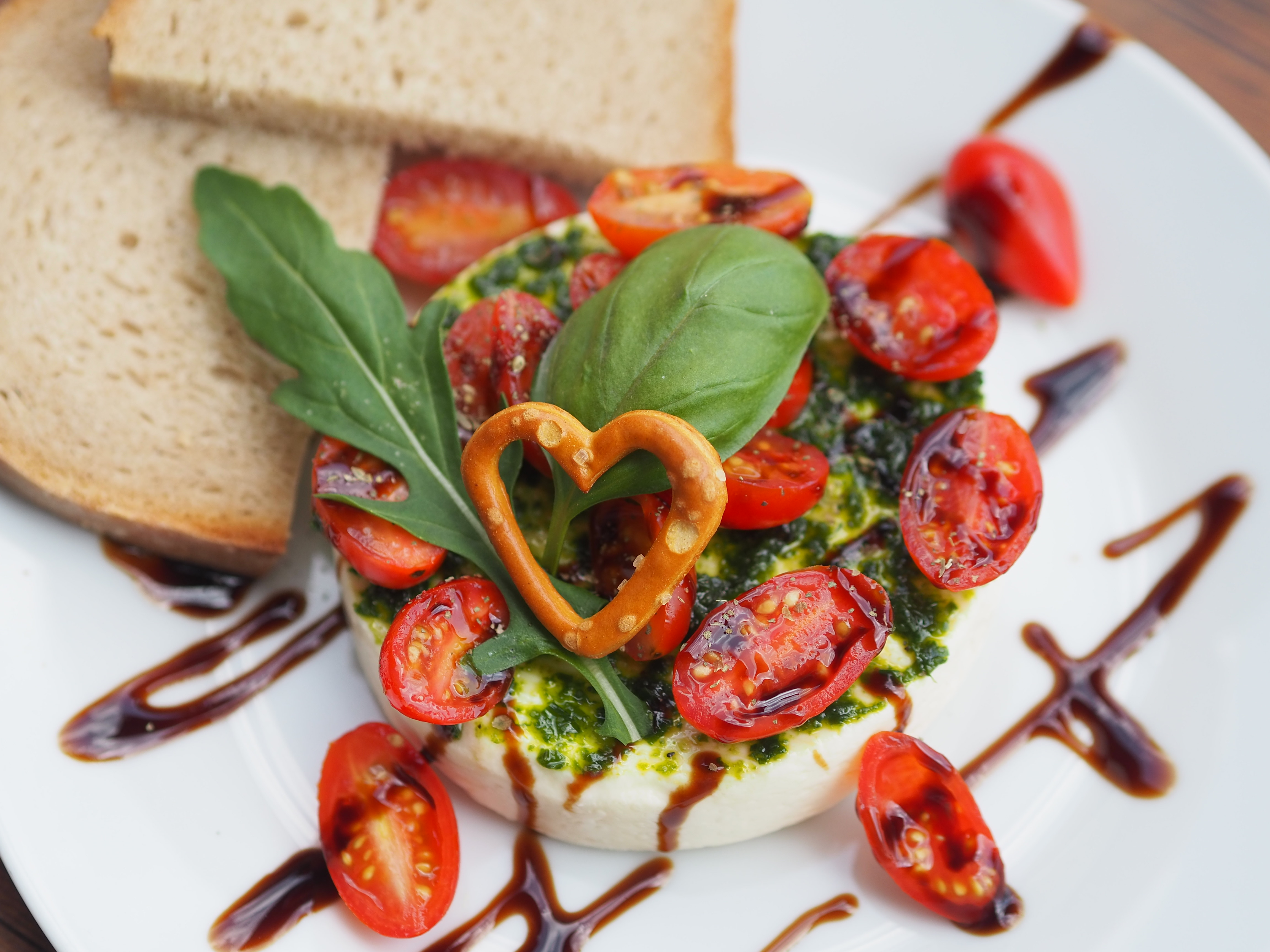 Nahaufnahme der Immer-andersBrotzeit. Auf Teller angerichteter Weichkäse mit Tomaten, Pesto und Brotscheiben. Ein Rezept einer Alpe in den Hörnerdörfern im Allgäu.