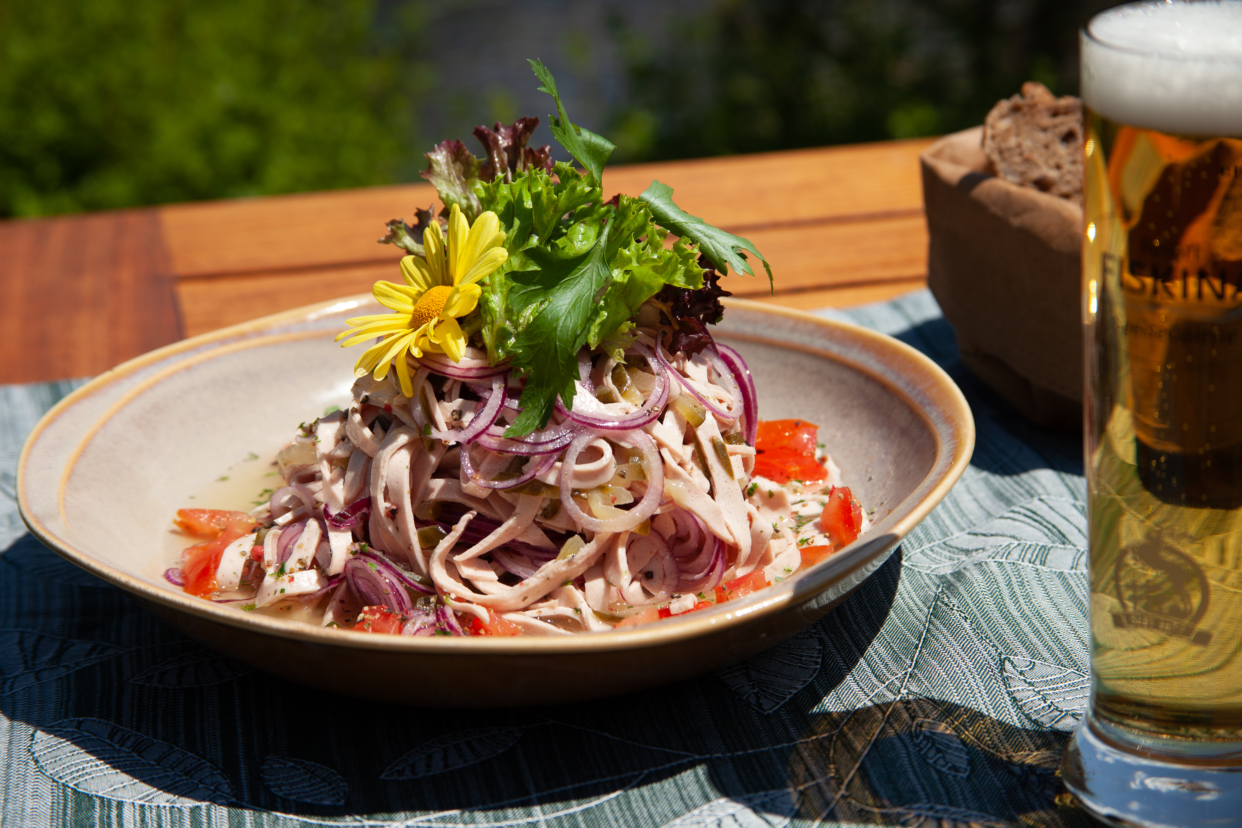 Allgäuer Wurstsalat Wurstsalat mit Kräutern und Blüten garniert in einer Schüssel auf dem Holztisch, daneben ein helles Bier.