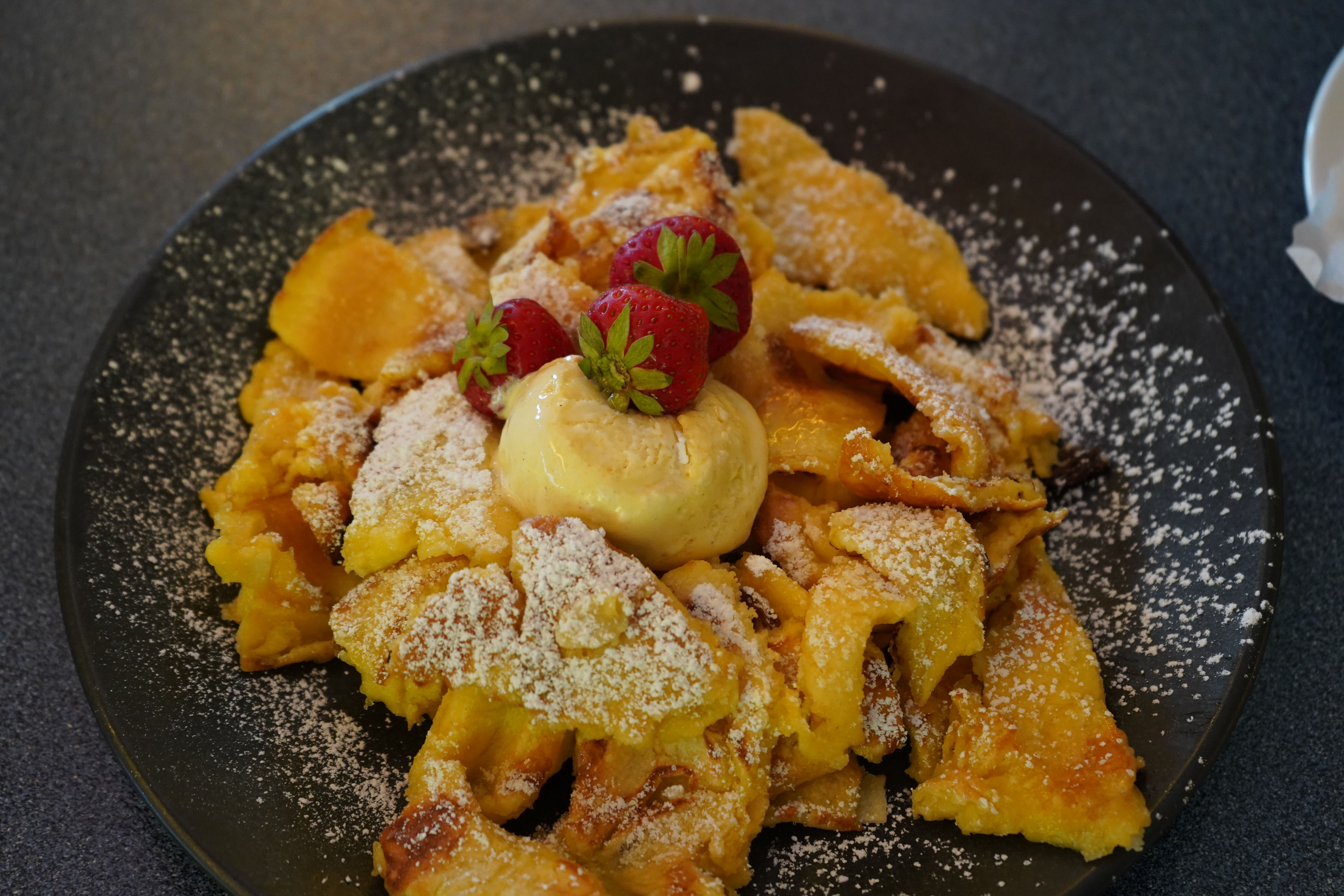 Teller mit Allgäuer Kaiserschmarrn und Vanilleeis, garniert mit Erdbeeren.