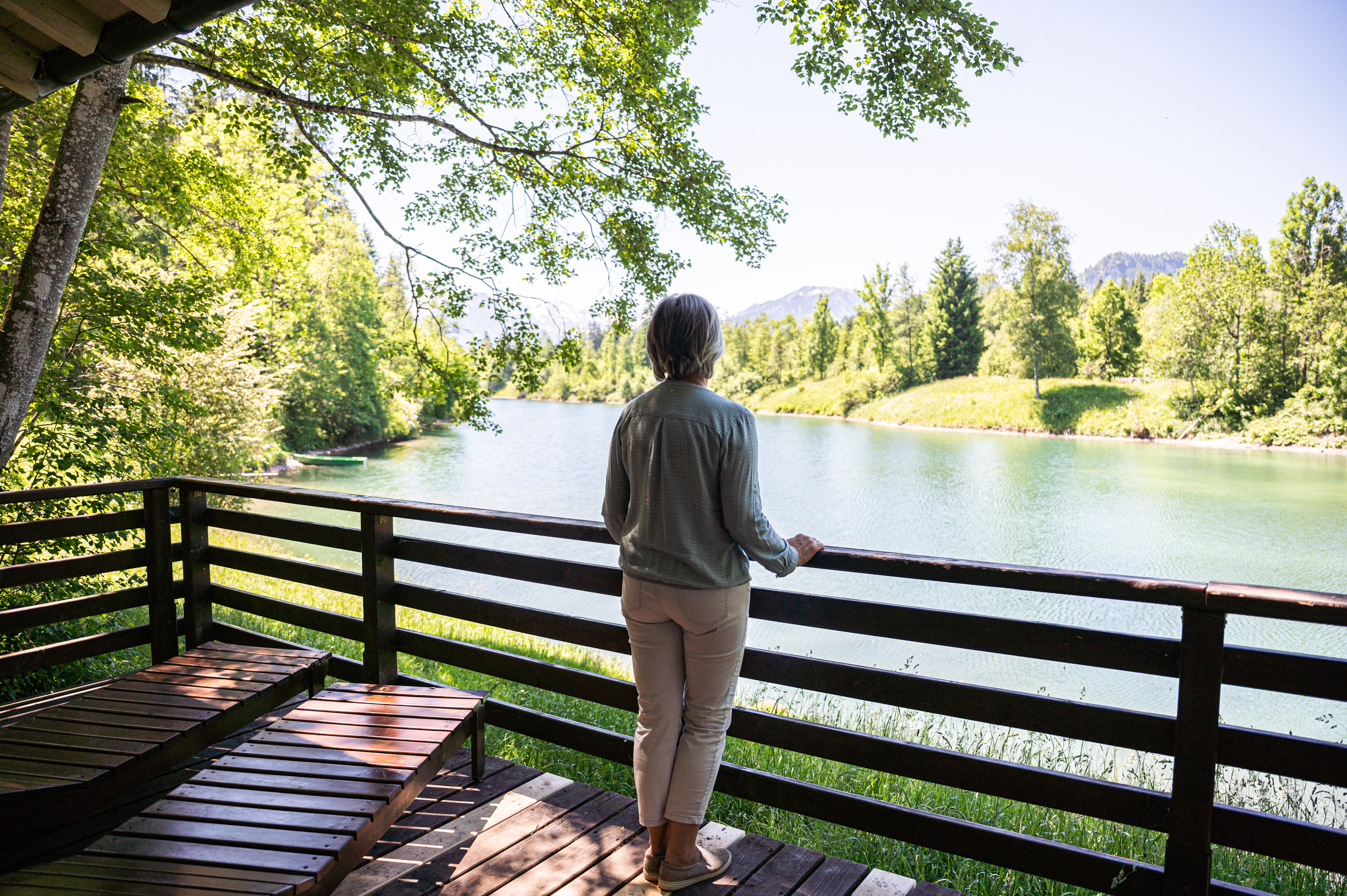 Frau steht am Geländer des Ruhepavillons und blickt auf den Auwaldsee in Fischen