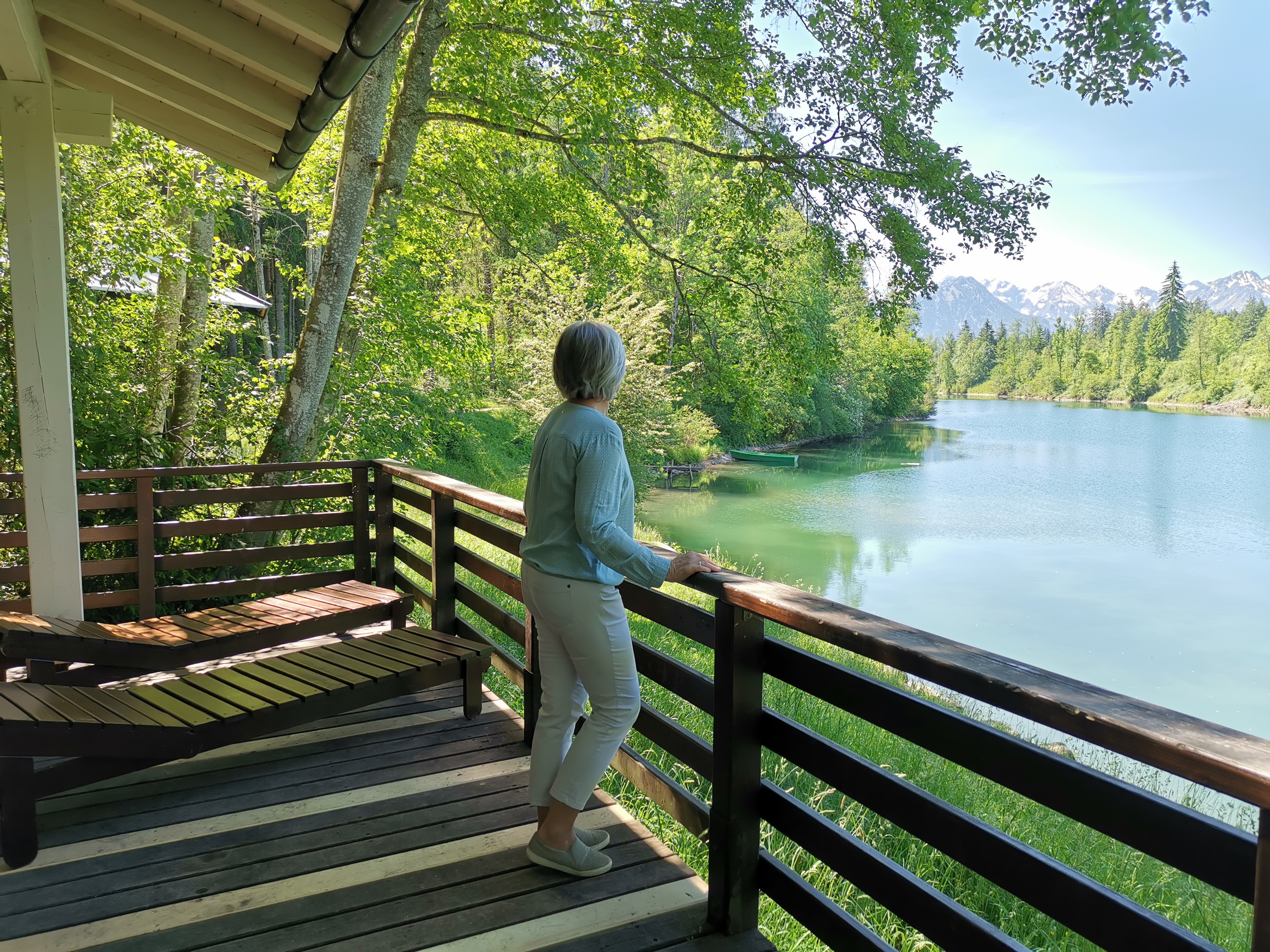 Person steht am Geländer des Ruhepavillons am Auwaldsee in Fischen und blickt auf das Wasser