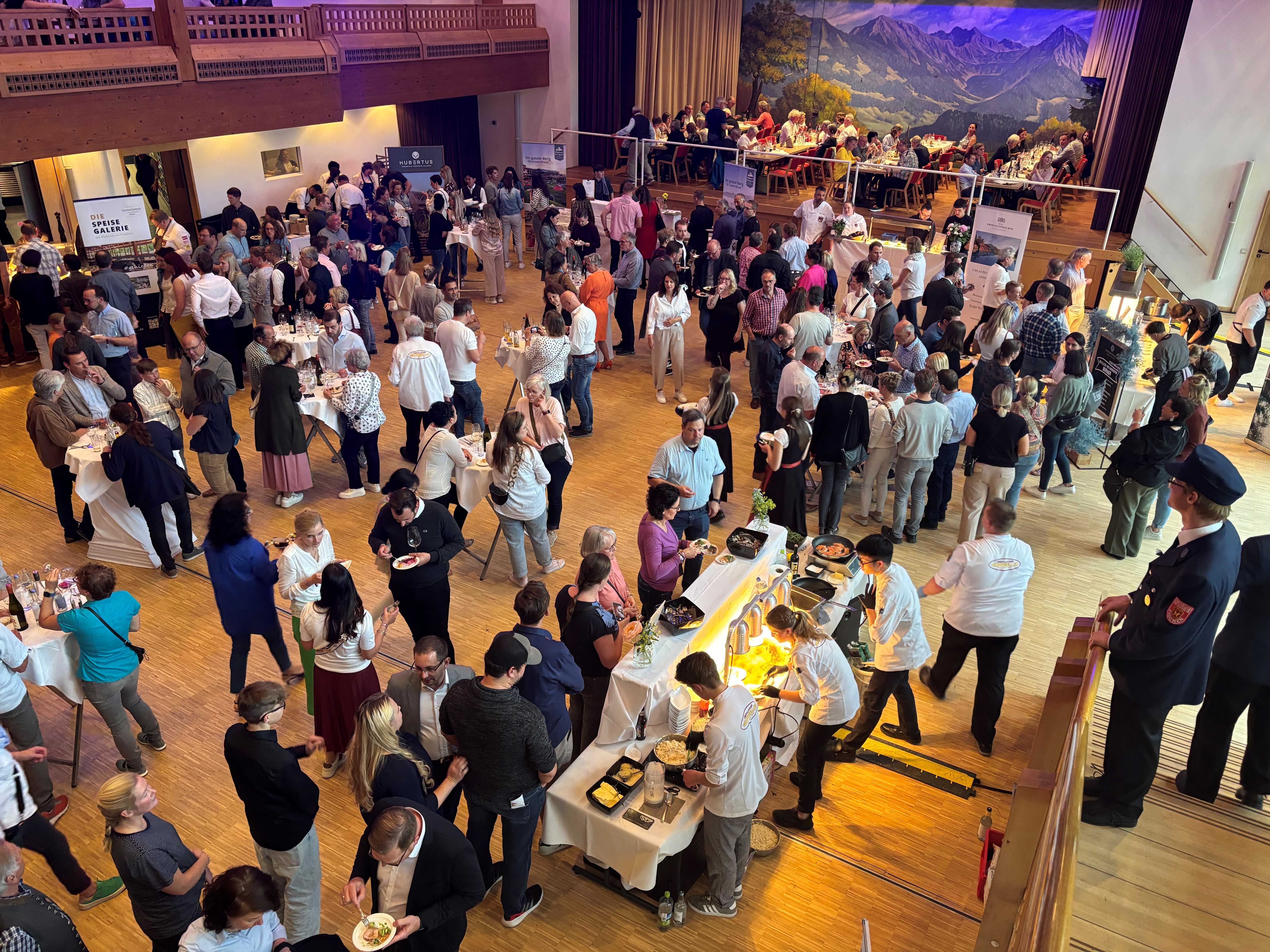 Viele Personen essen an Stehtischen und stehen am Buffet an, beim Walking Dinner der kochenden Sterne im Kurhaus Fiskina in Fischen.