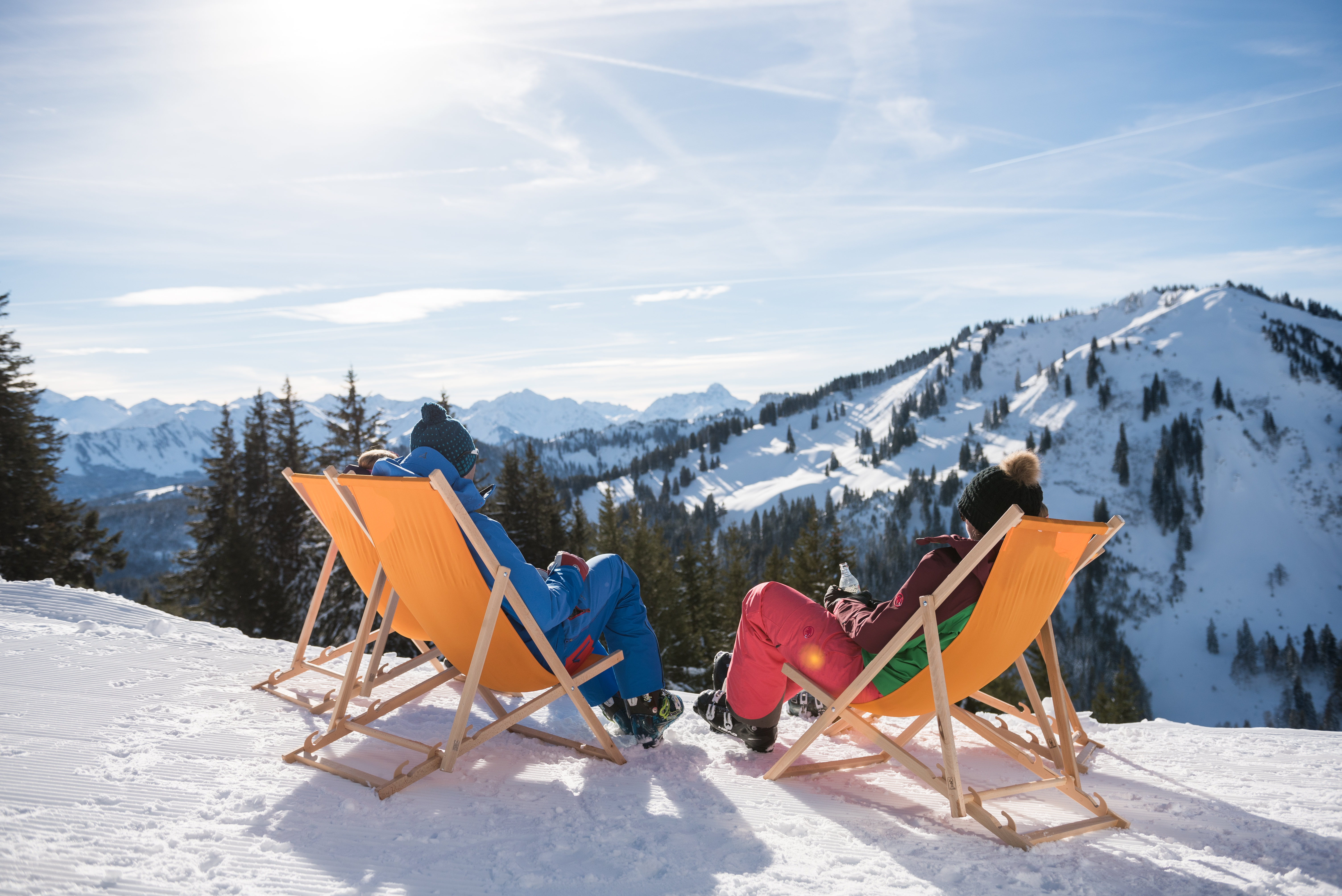 Zwei Menschen liegen im Liegestuhl mit Blick auf den verschneiten Gipfel des Wannenkopfes im Allgäu