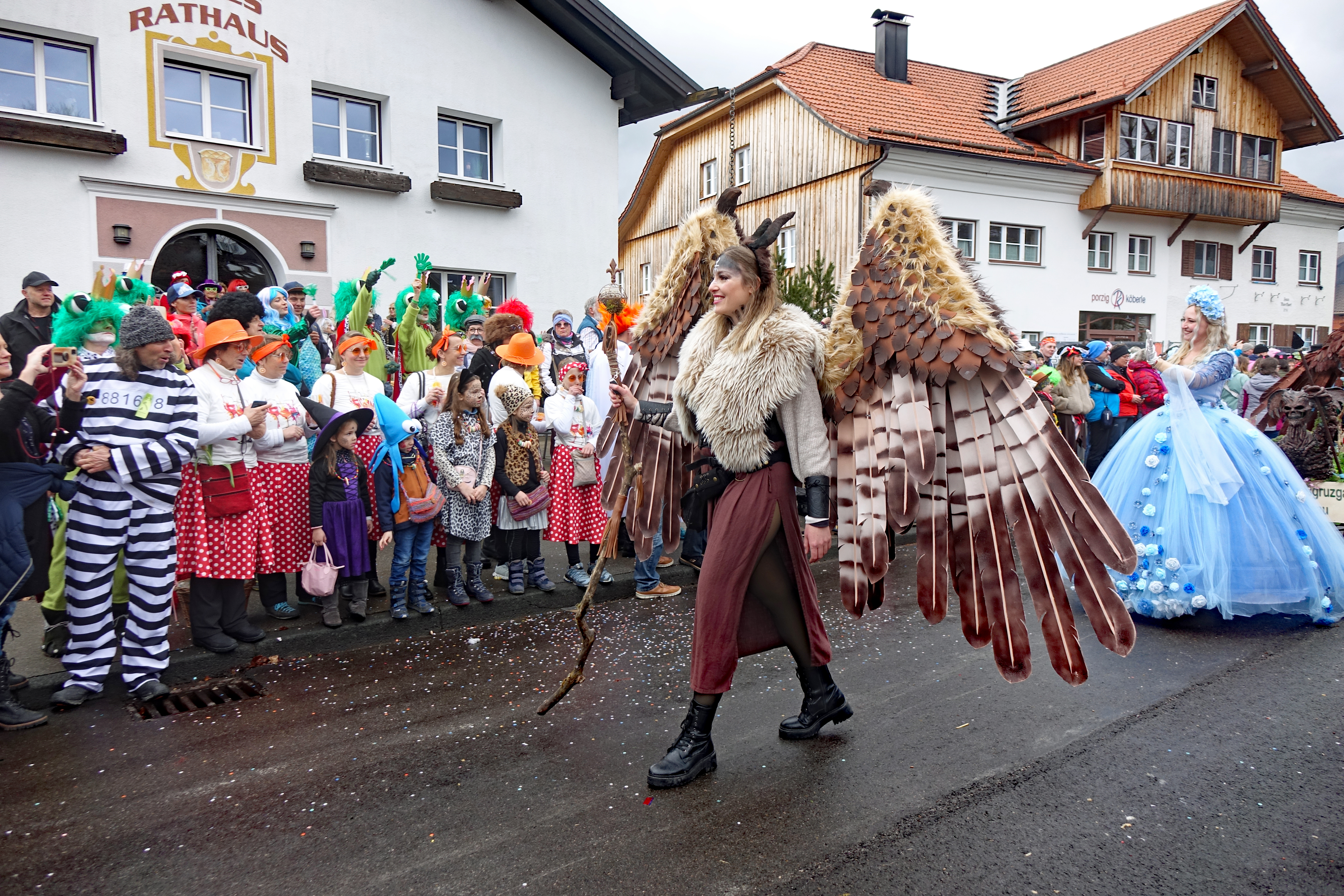 Faschingsumzug in Fischen, kostümierte Personen bestaunen am Straßenrand die als Greifvogel verkleidete Person des Faschingsumzuges