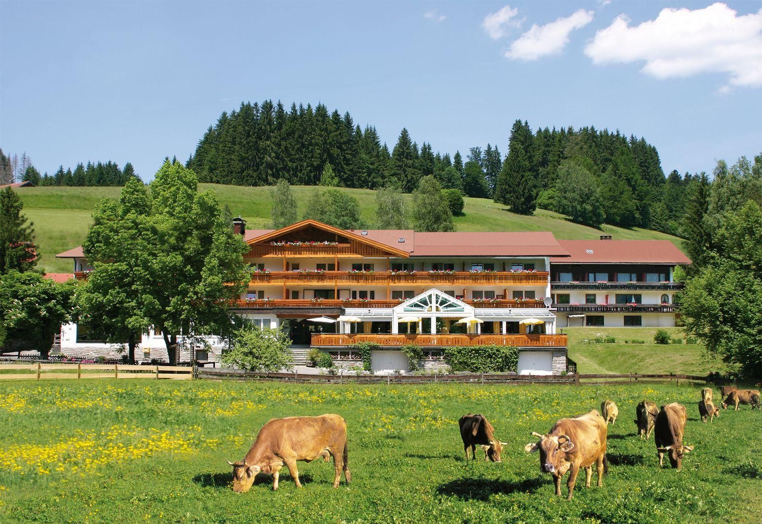 Das Hotel Sonnenbichl von der Ferne, im Vordergrund eine Weide im Frühjahr mit Kühen.