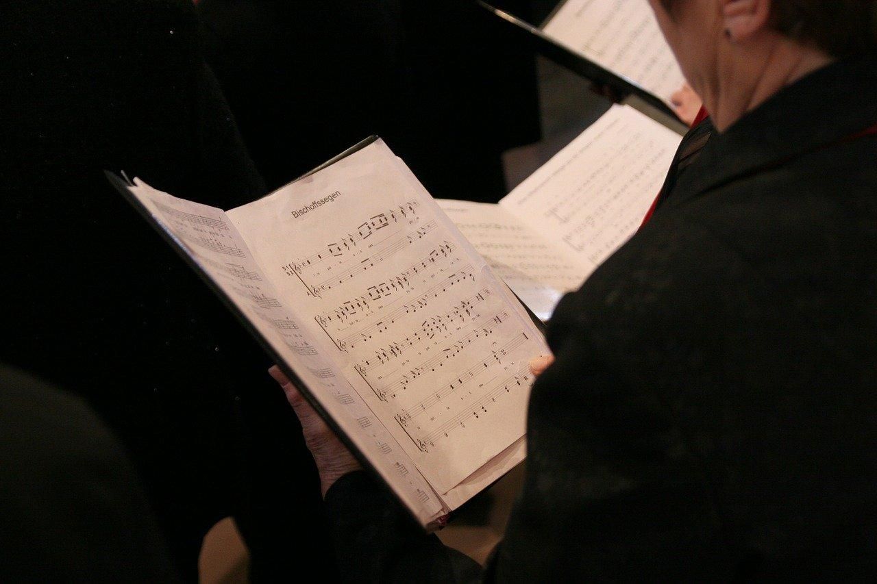 Eine Person im Chor hält Text und Noten des aktuellen Lieds in der Hand.