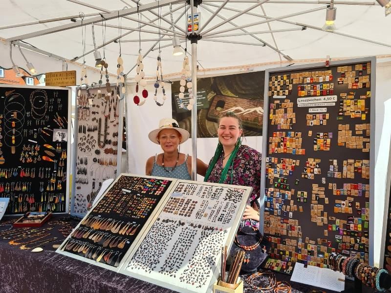 Ein Marktstand mit Perlenschmuck und im Hintergrund zwei Verkäuferinnen, die ihre Ware präsentieren.