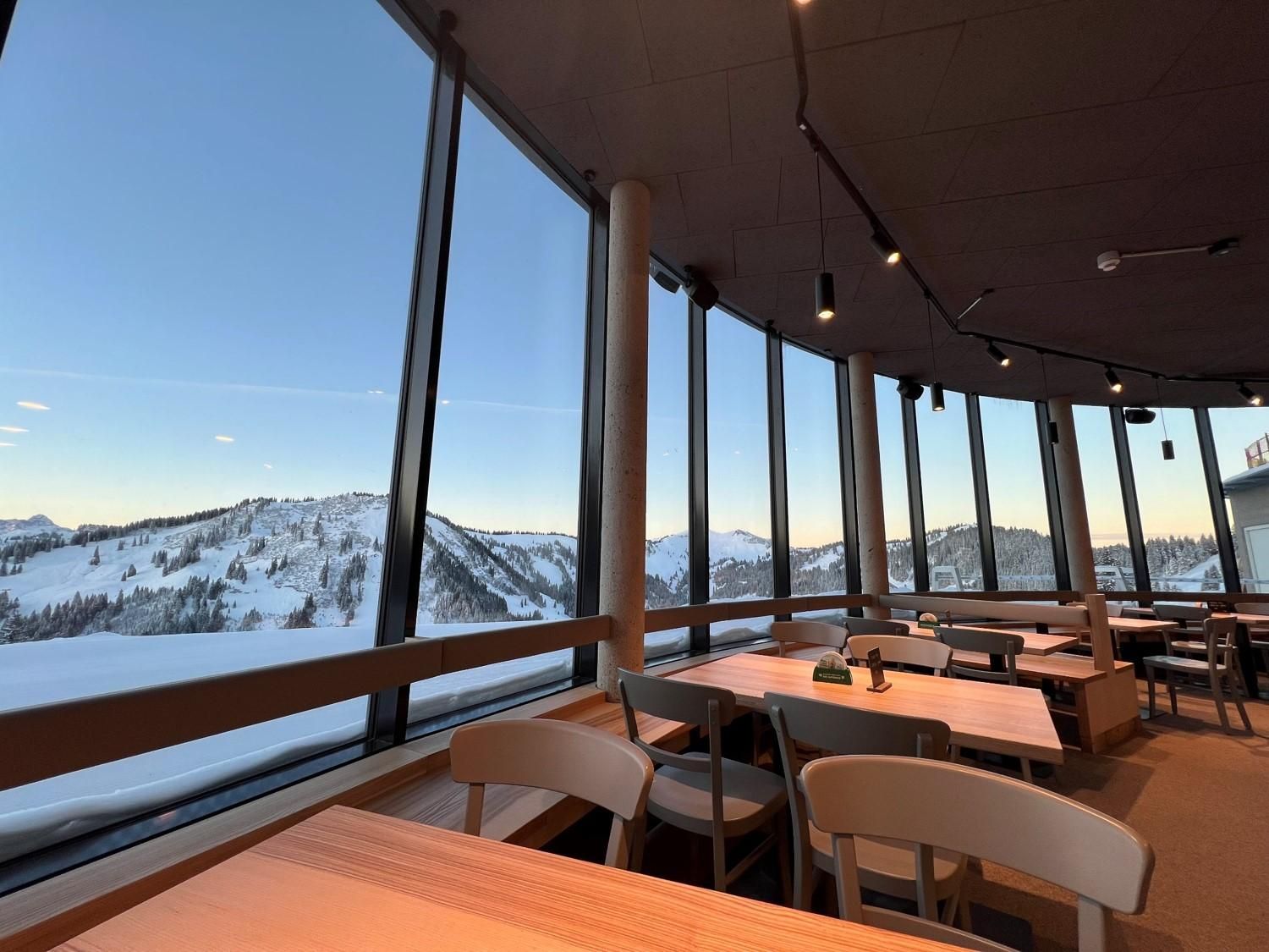 Gemütlicher Innenbereich mit Holztischen und Stühlen vor beeindruckenden Bergpanorama.