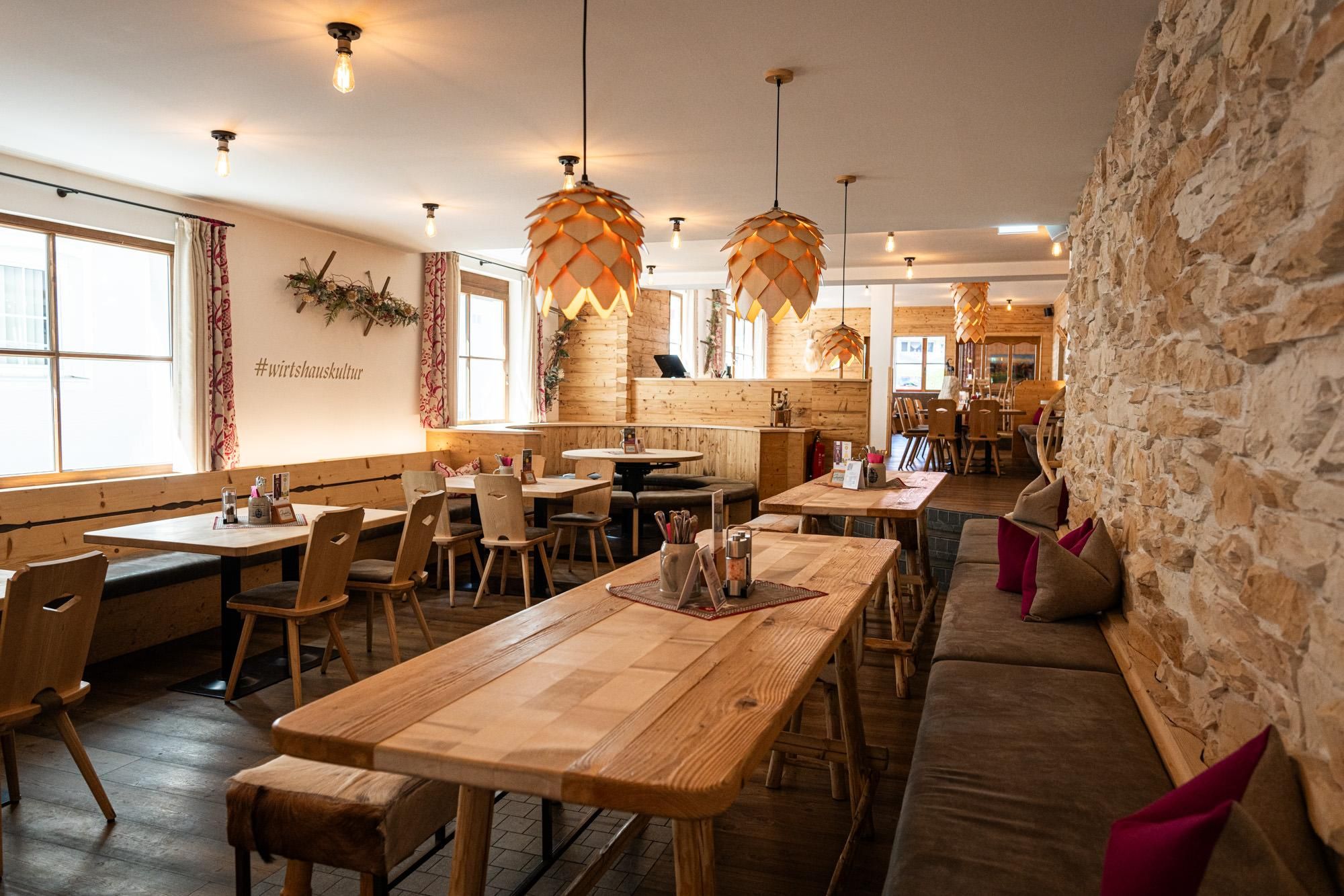 Das Restaurant mit Holztischen und einer hellen Natursteinwand.