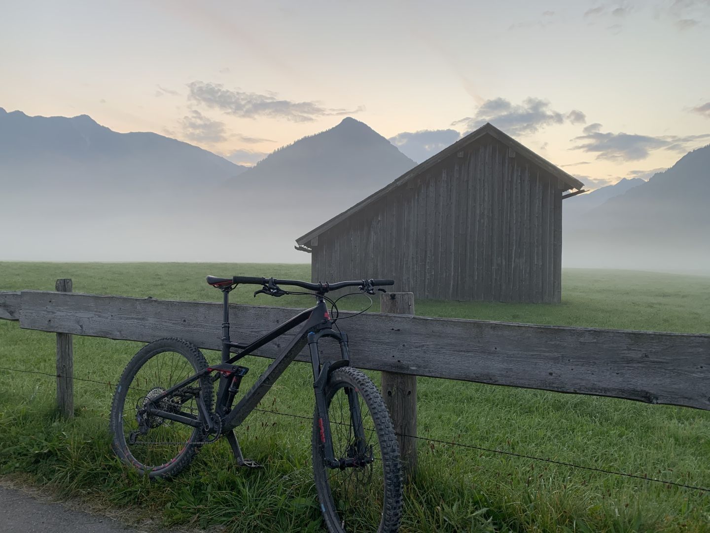 Ein Rad lehnt an einem Holzzaun vor einem Stadl bei morgentlichem Dunst