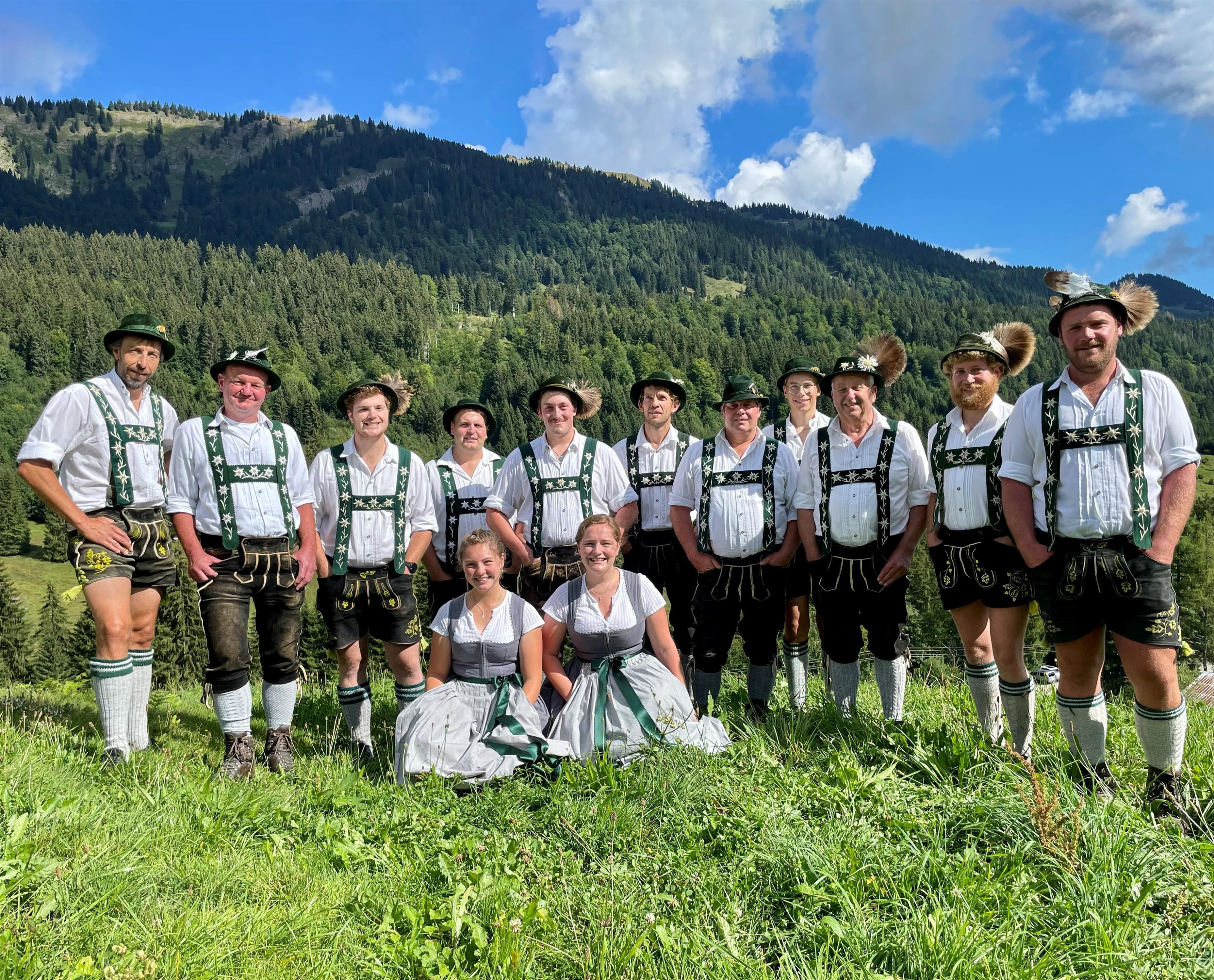 Gruppe in Tracht vor Berglandschaft. Männer in Lederhosen, Frauen in Dirndl.