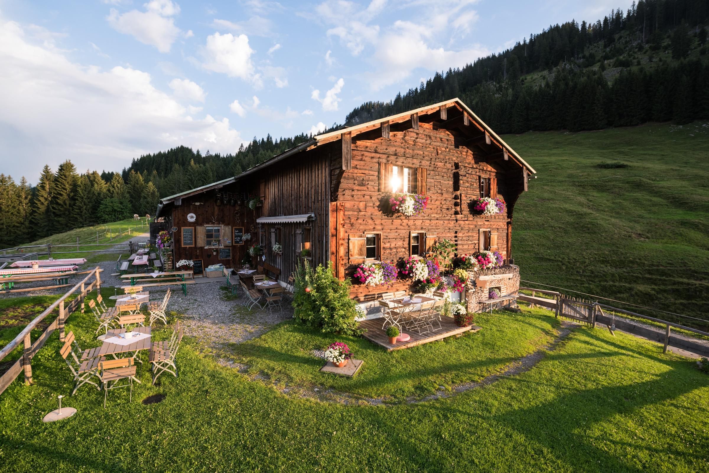 Holzhaus mit Blumenkästen an den Fenstern, Tische und Stühle im Außenbereich auf einer grünen Wiese.