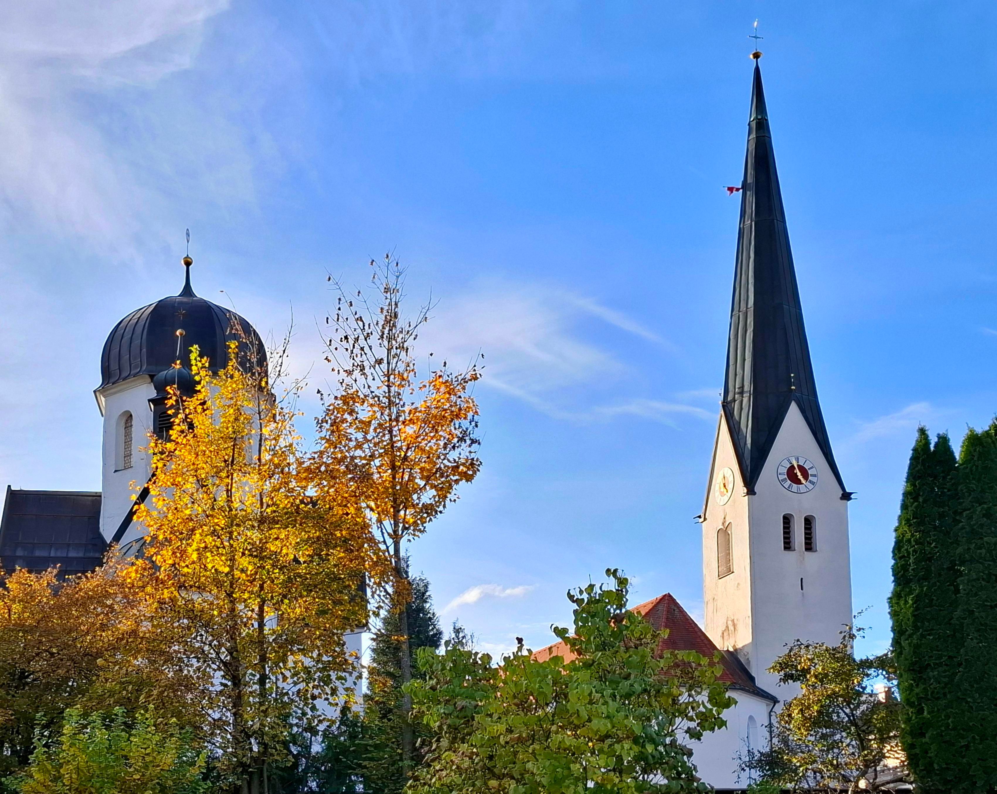 Die Pfarrkirche St. Verena in Fischen feiert im Jahr 2026 ihr 900-jähriges Jubiläum. Markant sticht der hohe gotische Kirchturm in die Luft. Daneben die wunderhübsche Kapelle in das Friedhofsarial mit eingebettet.