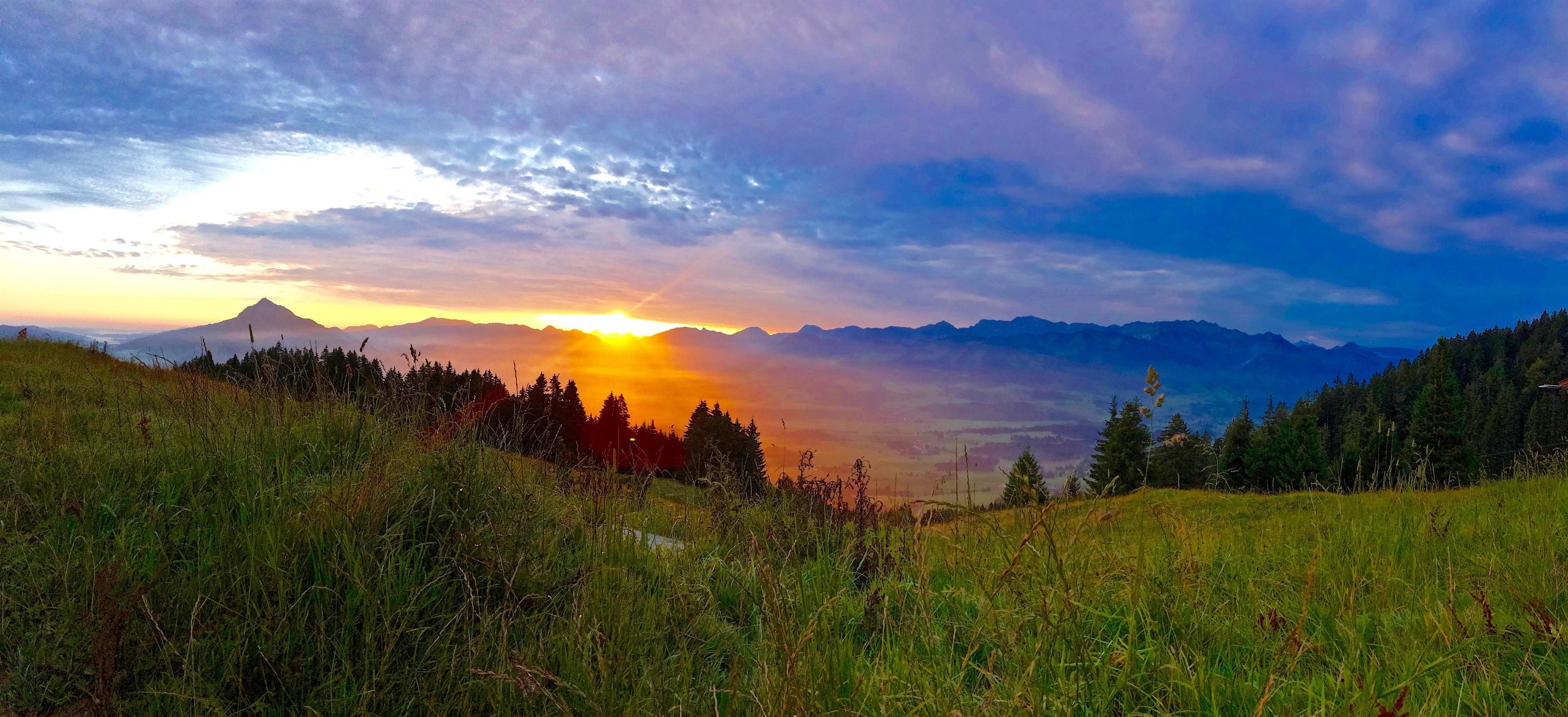 Ein malerischer Sonnenaufgang über den Bergen, mit orangerotem Himmel und einer nebelverhangenen Talsohle.