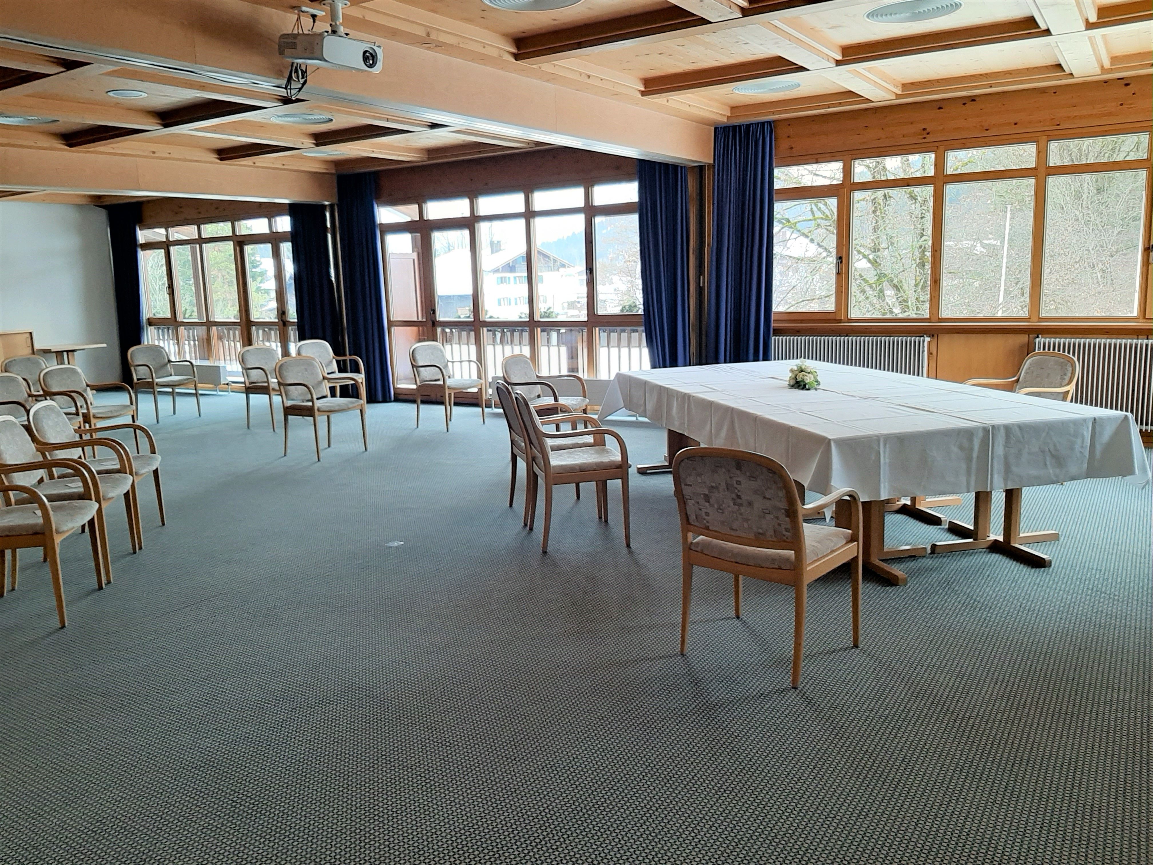 Großer mit Raum mit Trautisch mit weißer Decke und hellen Stühlen. Viele Fenster.