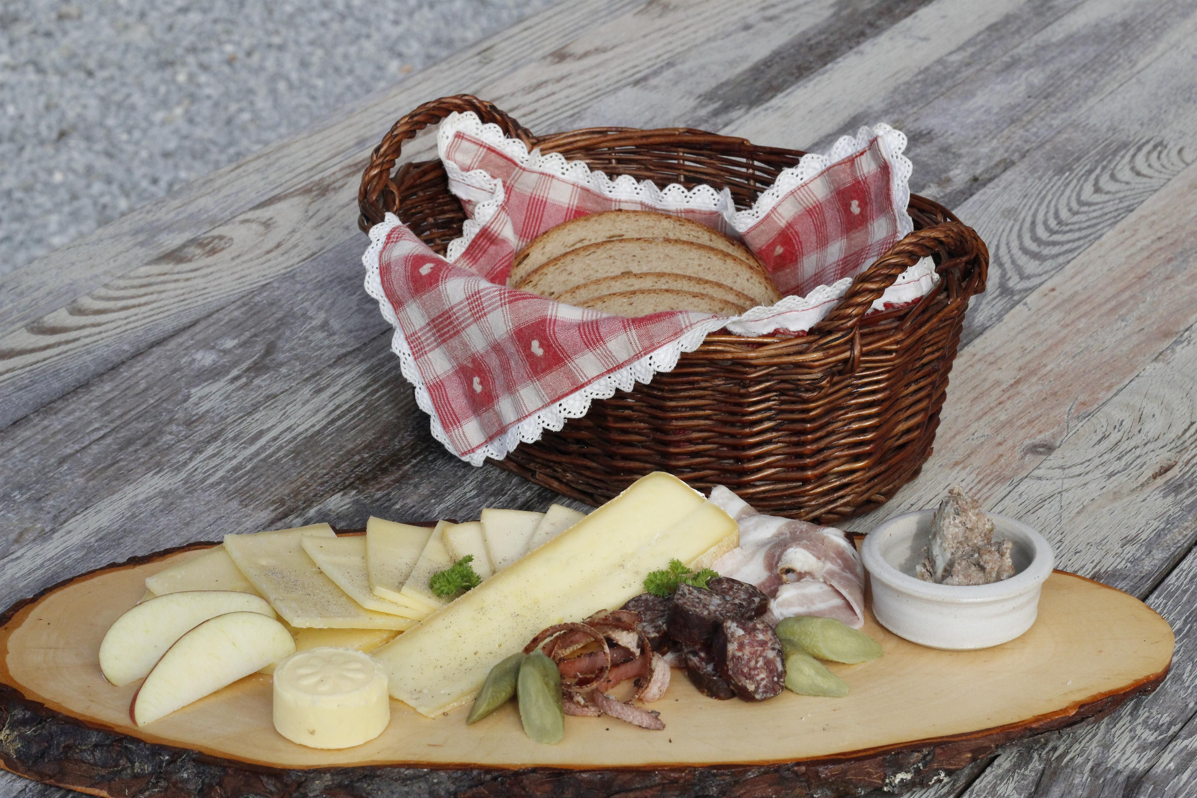 Auf einem Holztisch steht ein Korb mit Brot. Im Vordergrund liegt Käse und Wurst auf einem Holzbrett.