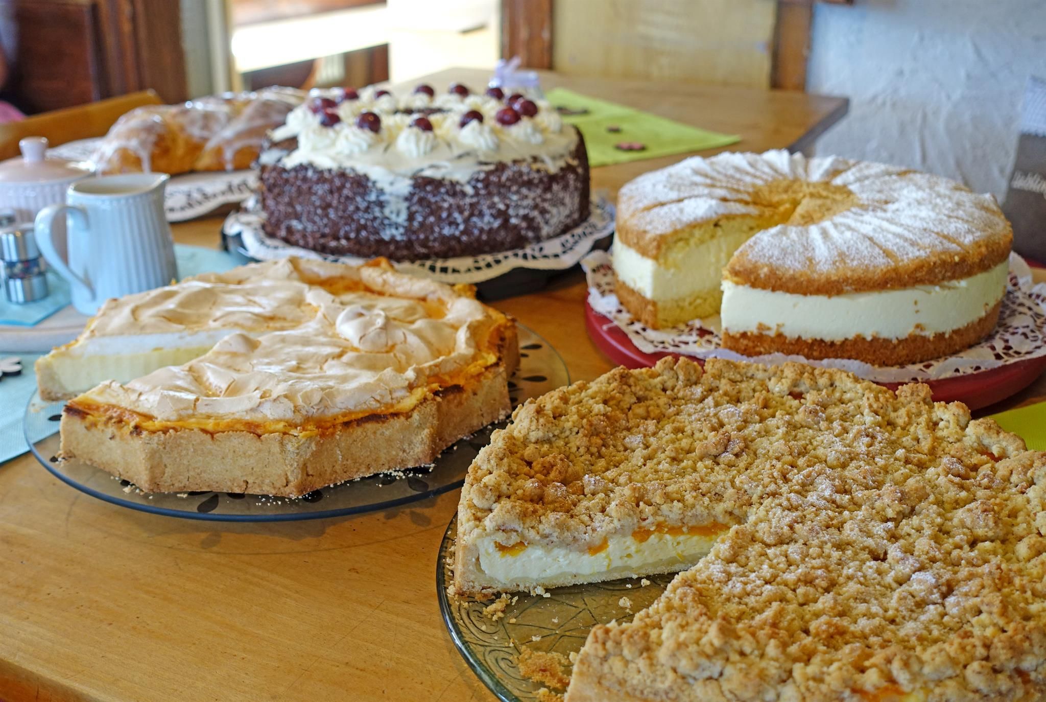 Vier verschiedene Kuchen auf Glastellern auf einem Holztisch.