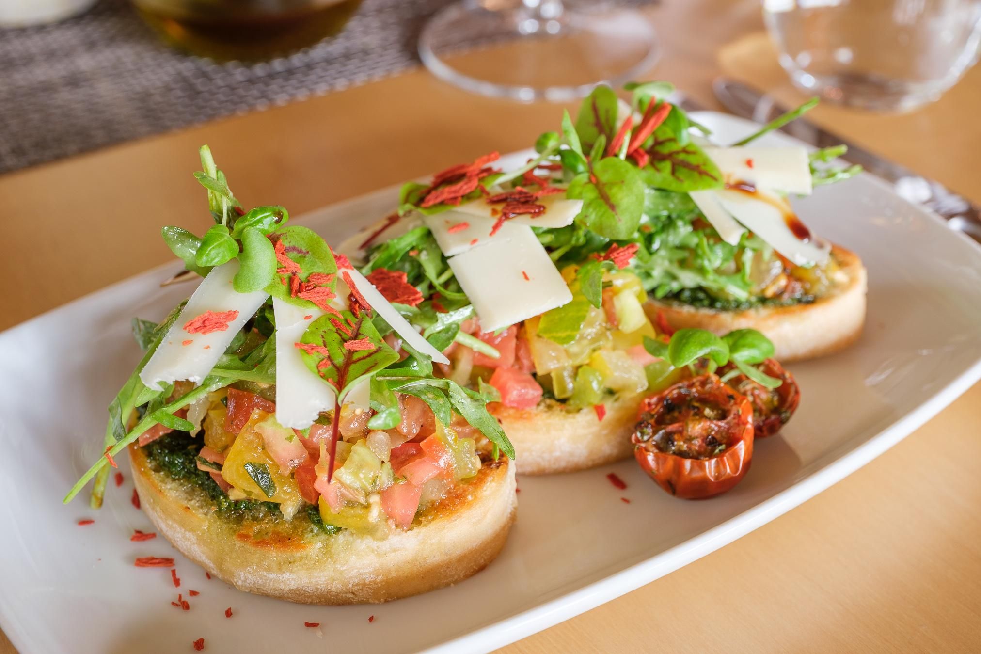 Drei Bruschetta auf einem Teller: geröstetes Brot mit Tomaten, Ruccola, Parmesan und getrockneten Tomaten.