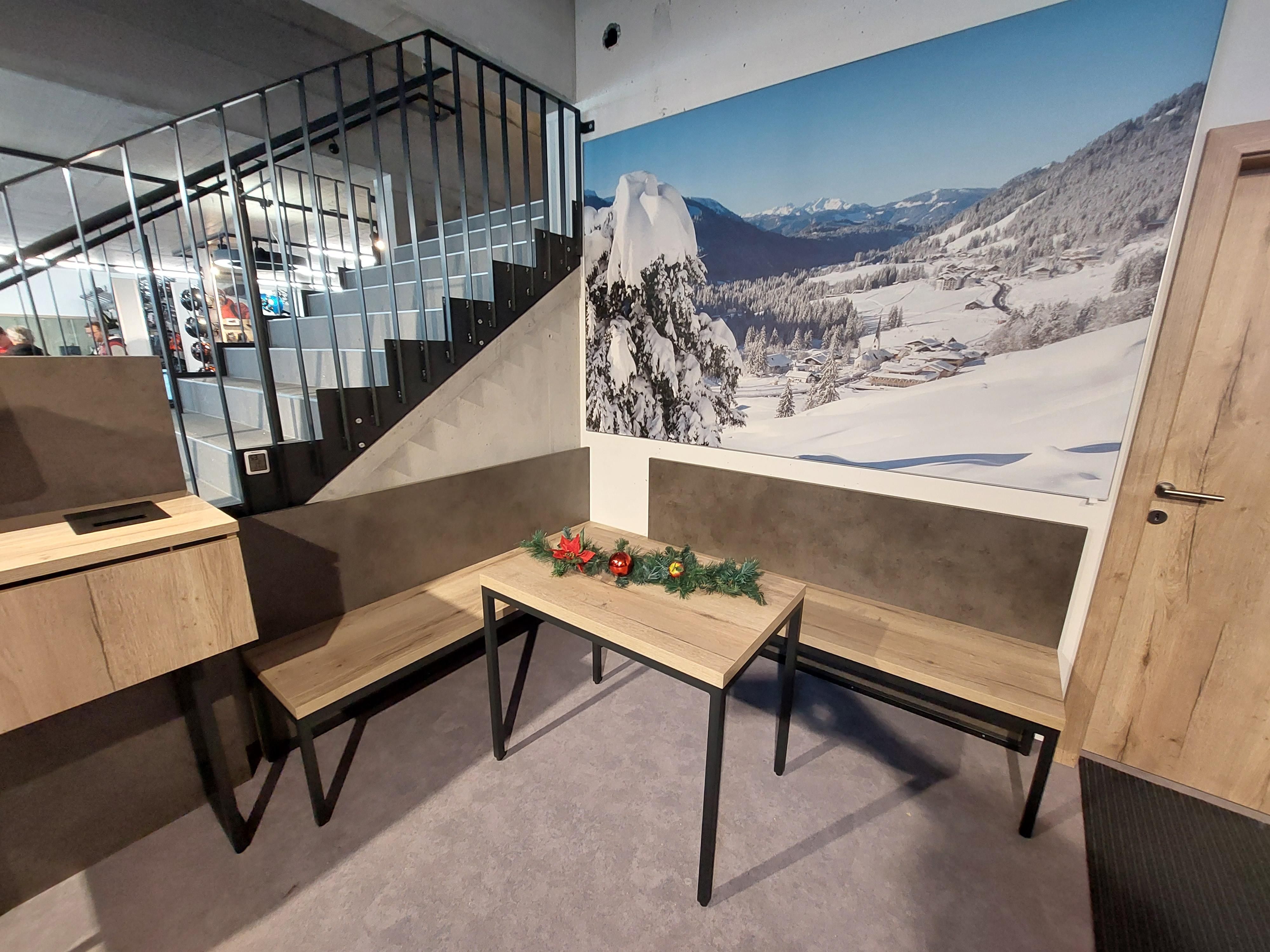 Sitzecke mit Holztisch und Bänken. Wandtapete mit Winterlandschaft. Dekoration mit Tannengrün und roten Kugeln auf dem Tisch. Treppe im Hintergrund.