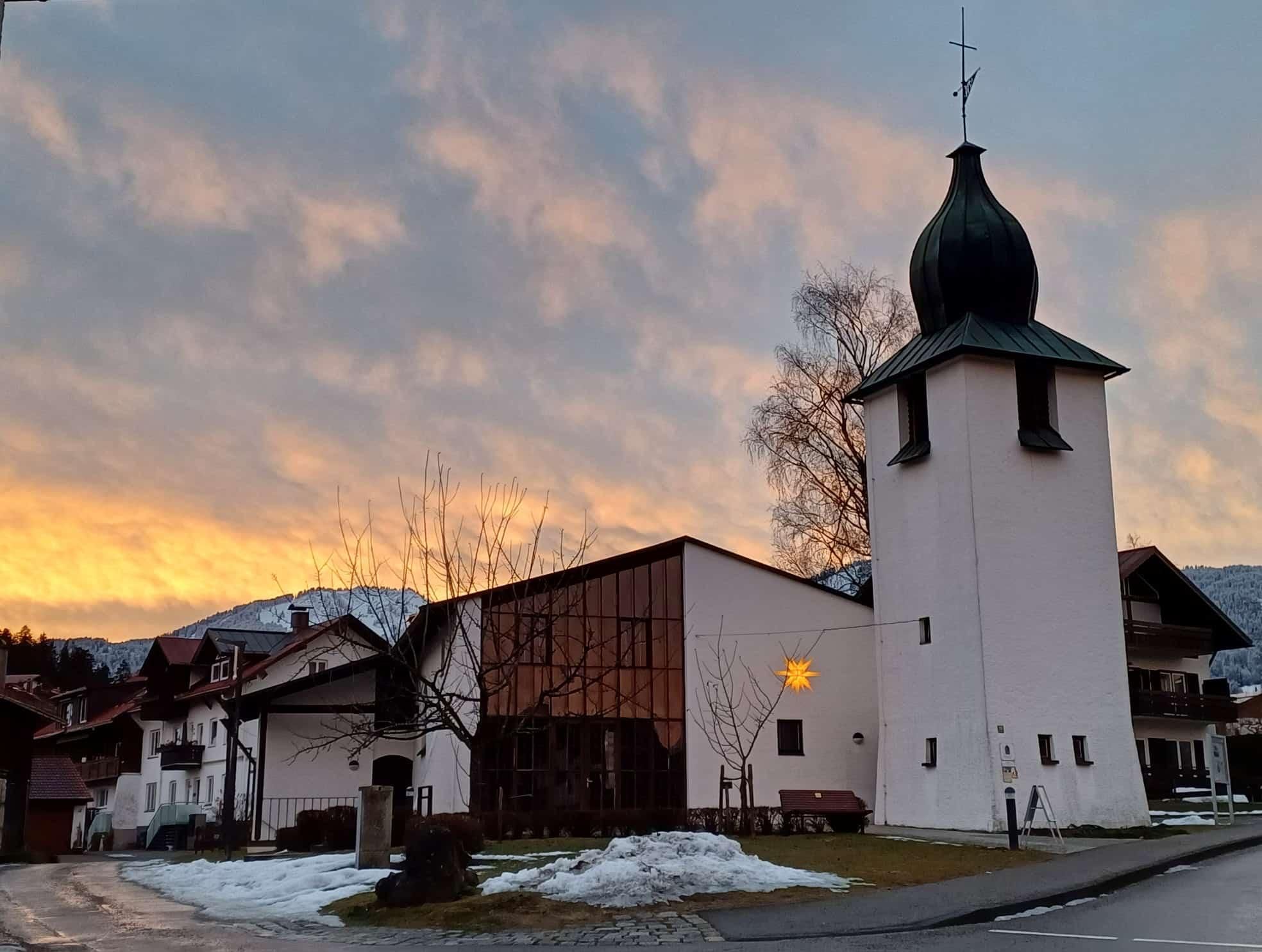 Die Kirche "Zum Guten Hirten". Der Himmel leuchtet in warmen Farben bei Sonnenuntergang.