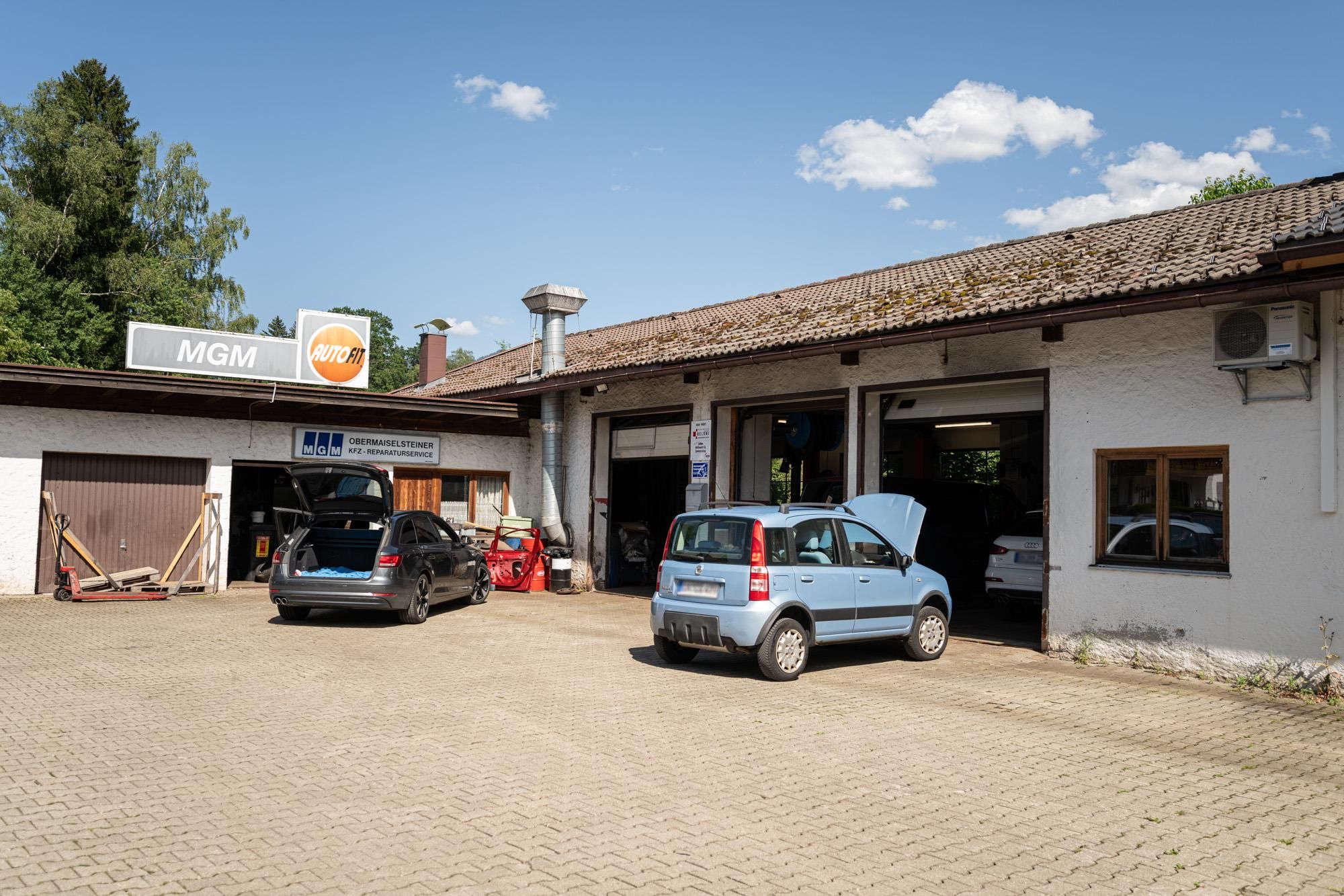 Vor der MGM-Werkstatt in Obermaiselstein stehen zwei Autos, im Hintergrund das Gebäude mit "MGM Autofit"-Logo.