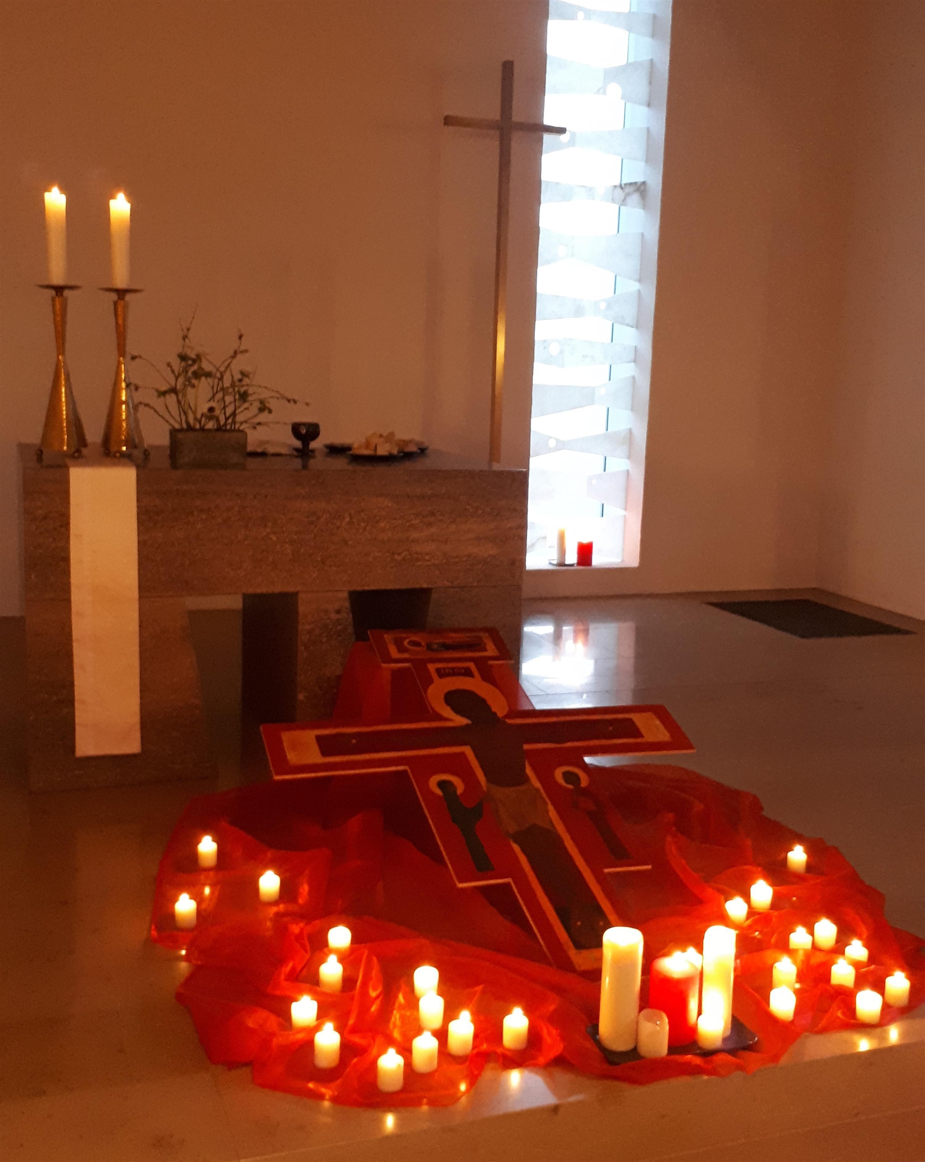Dekoration vor dem Altar mit Kreuz und vielen Kerzen und Lichtern auf einer roten Decke.