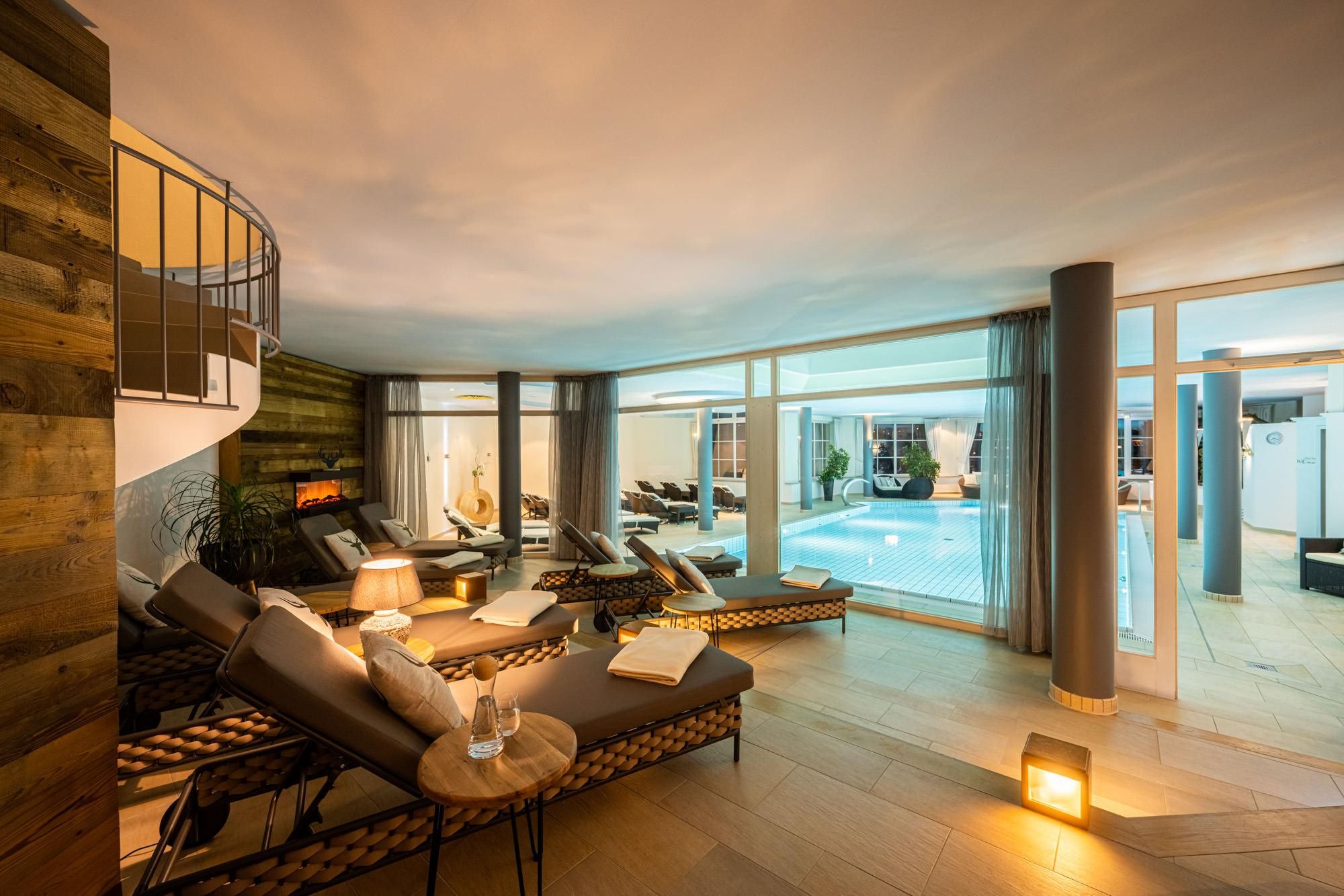 Ein eleganter Ruhebereich mit Liegen und einem Innenpool. Große Fenster sorgen für eine helle und einladende Atmosphäre.