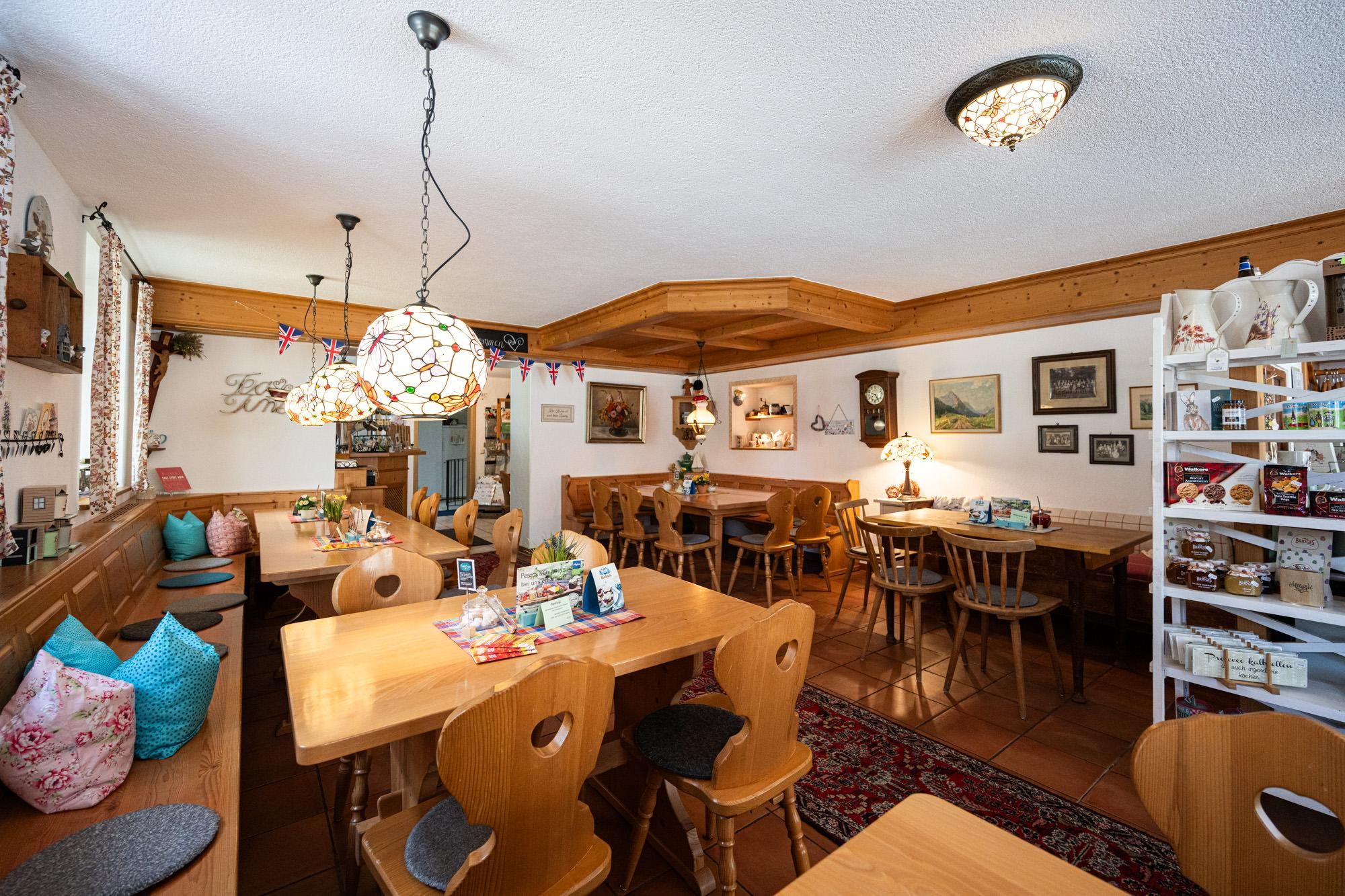 Der Gastraum: Tische, Stühle und Bänke aus Holz, alle Lampen im Tiffany-Stil, rechts ein Regal mit Geschenken.