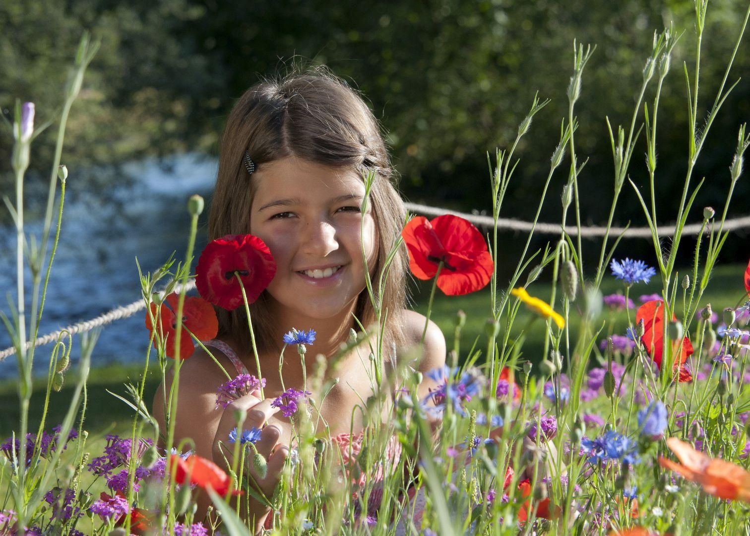 Ein Mädchen sitzt in einer Wiese mit bunten Blumen wie Mohn und Kornblumen.