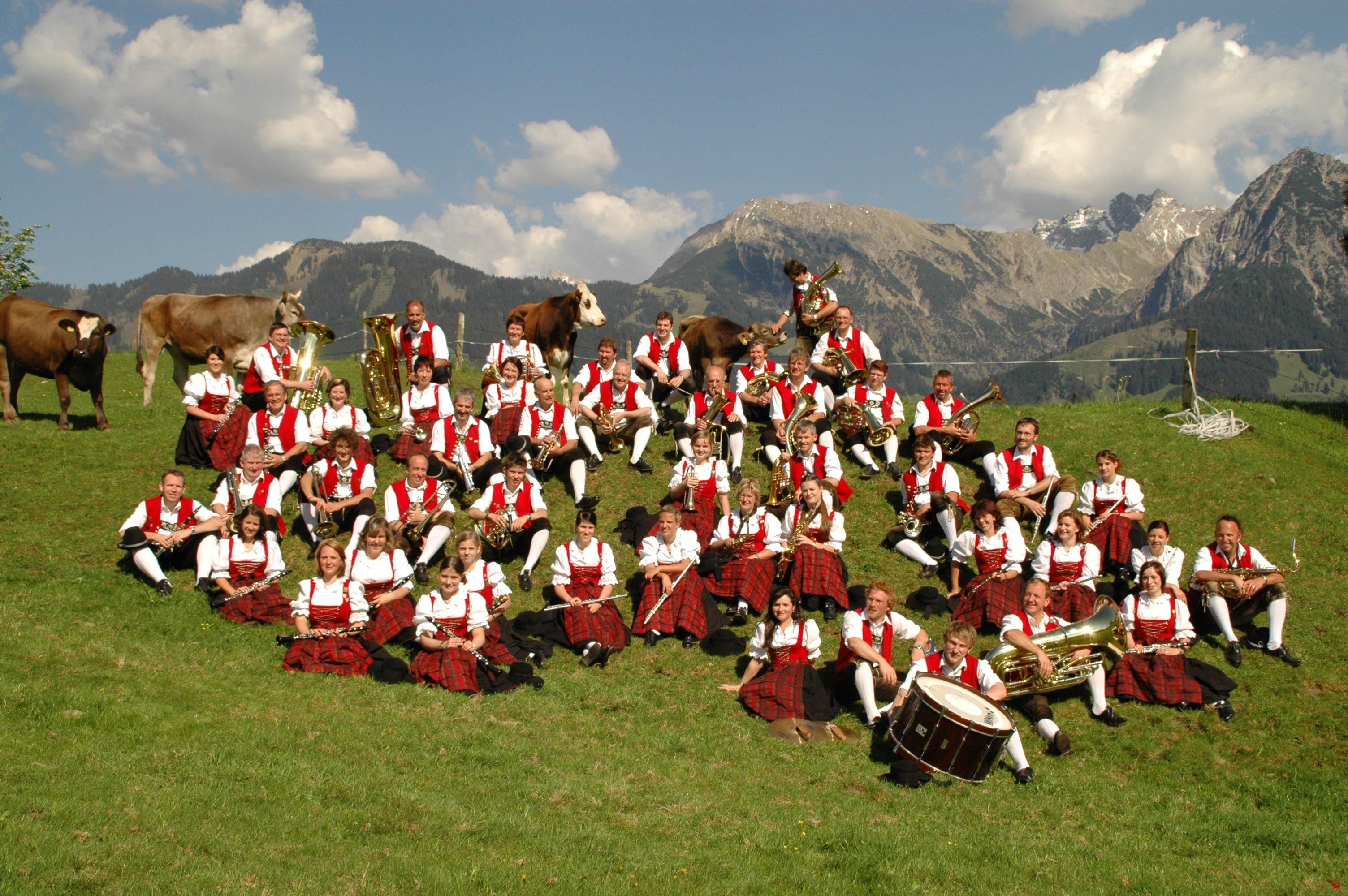 Foto von oben: die Blaskapelle Fischen auf einer Wiese, mit roten Westen oder Dirndloberteilen, die Insturmente dabei.