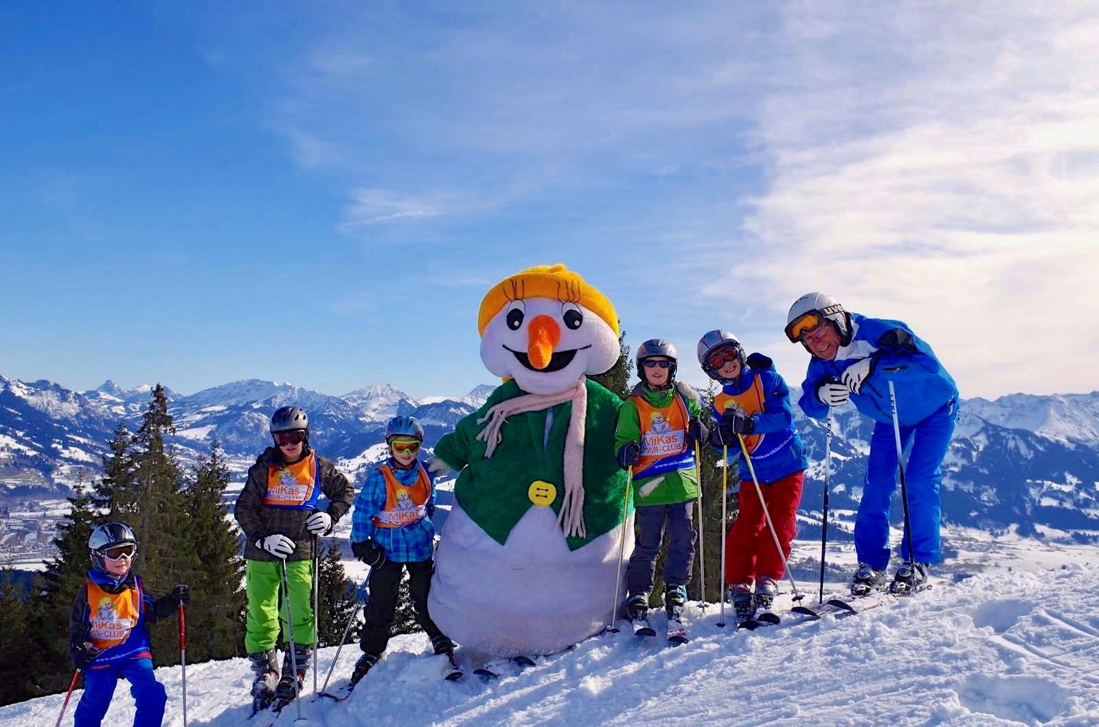 Eine Gruppe von Kindern mit Skilehrern und einem Schneemann-Maskottchen posiert im Schnee.