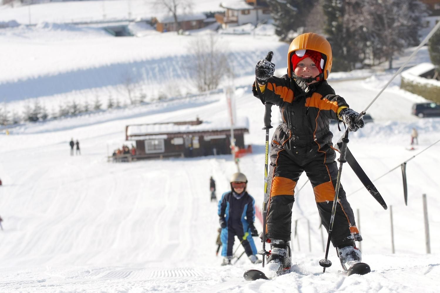 Ein Kind mit orangefarbenem Helm und Skibrille fährt Ski auf einer verschneiten Piste.
