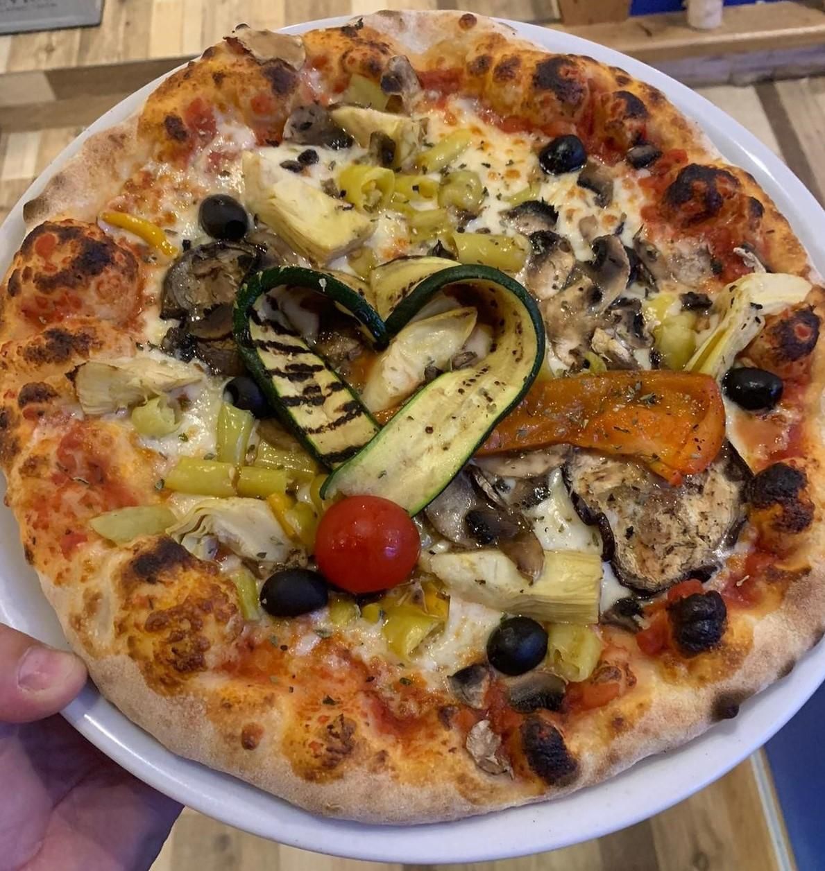 Eine Pizza mit Gemüse wie Oliven und Auberginen, zwei gebratene Zucchinischeiben formen ein Herz in der Mitte.