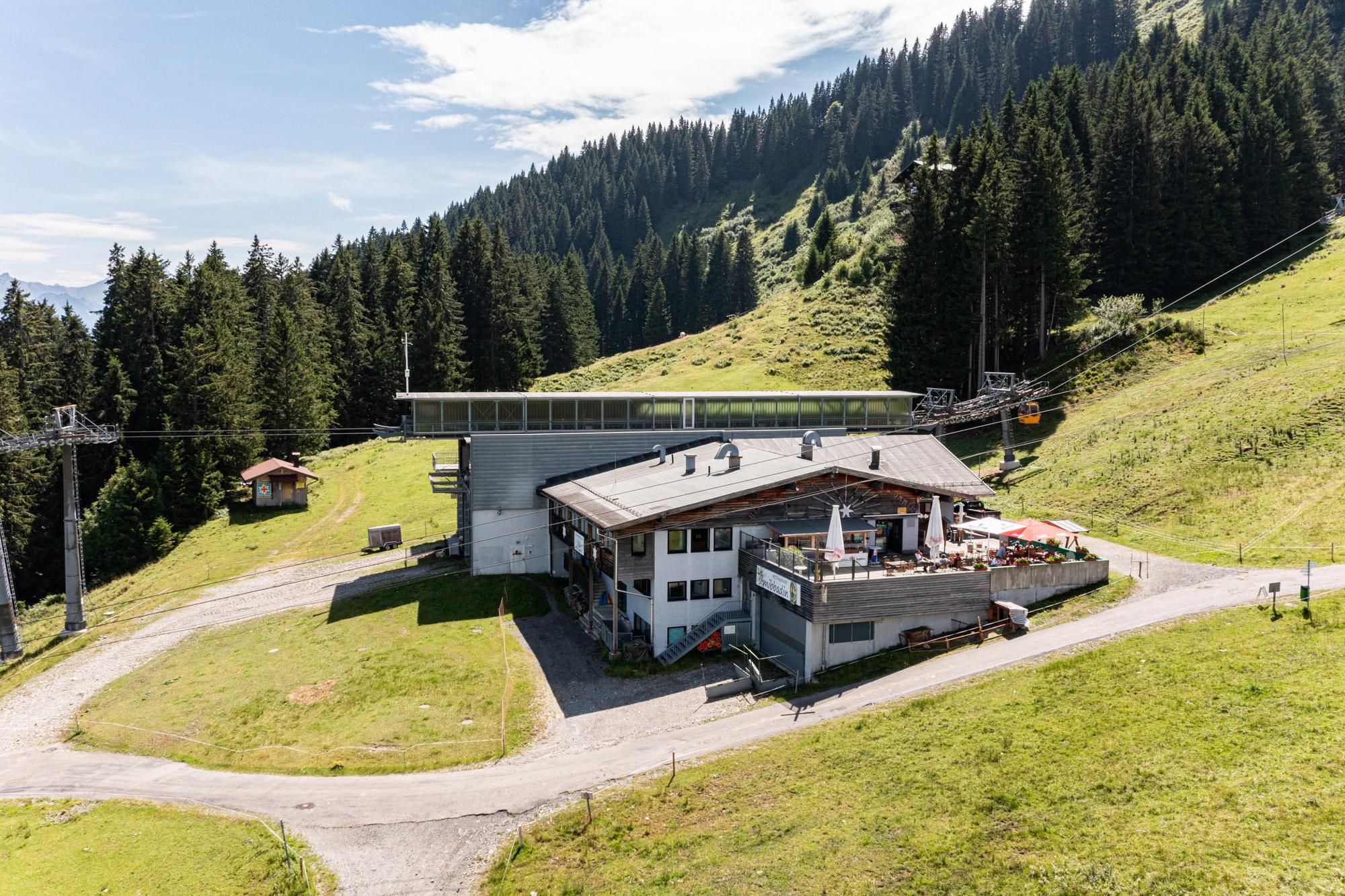 Moderne Mittelstation der Weltcup-Express Sesselbahn. Umgeben von grünen Berghängen und dichten Wäldern.