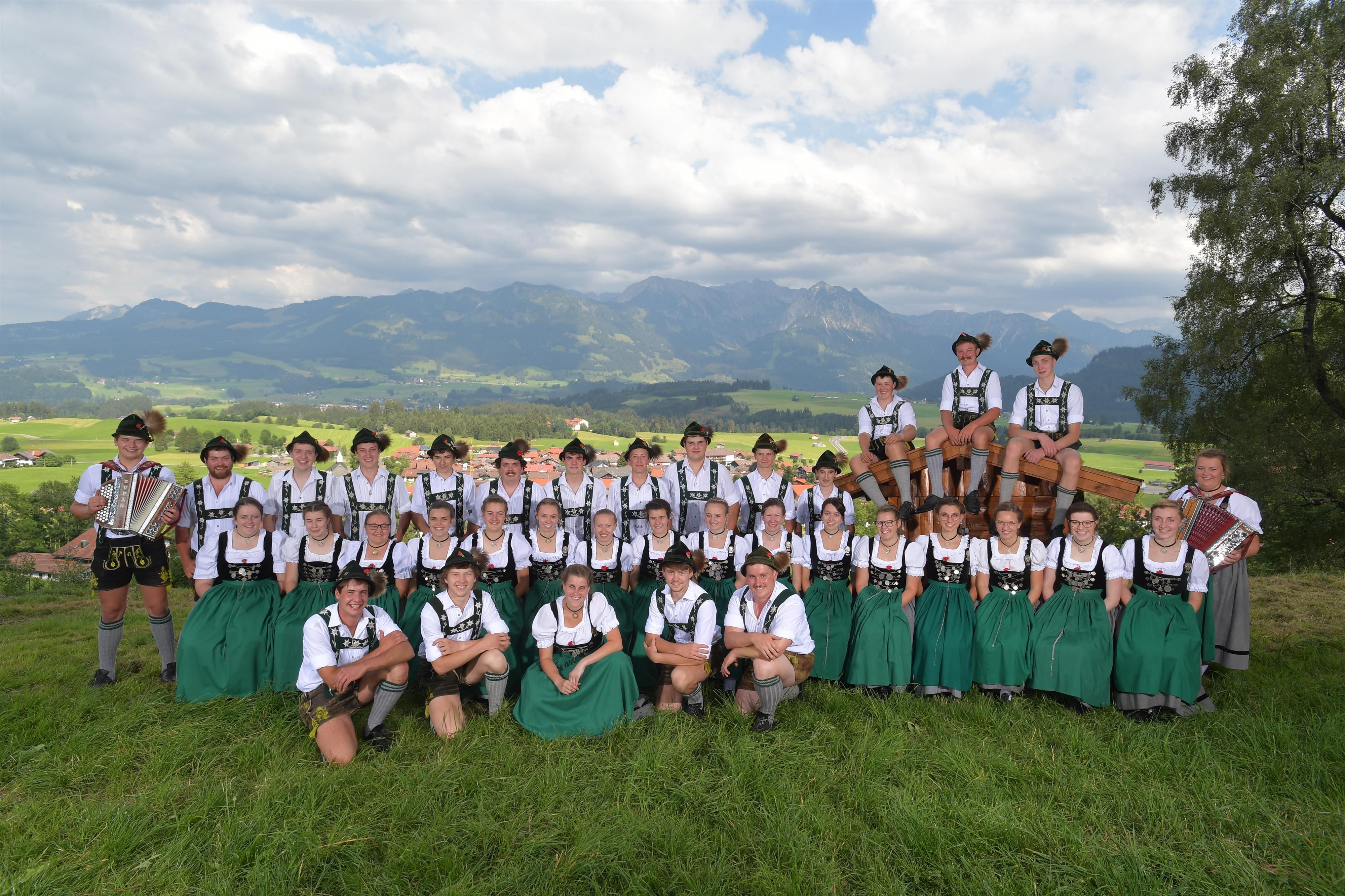Große Gruppe der Bolsteranger Plattlar in Tracht, posierend auf einer grünen Wiese.  Bergpanorama im Hintergrund.