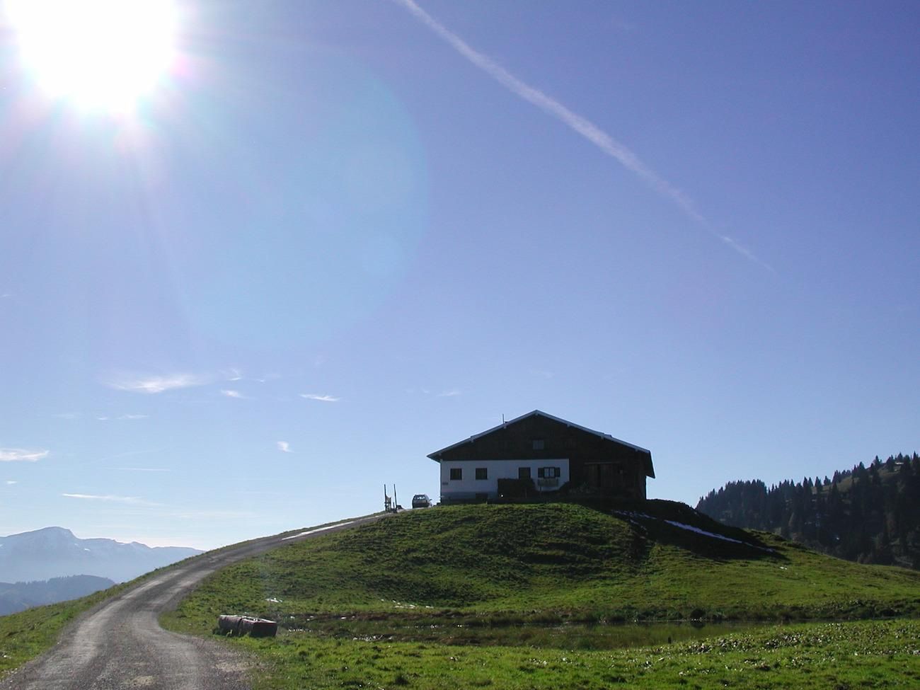 Die Alpe Spicherhalde bei Balderschwang thront auf einem grünen Hügel. Ein Wanderweg führt zur Hütte hinauf.