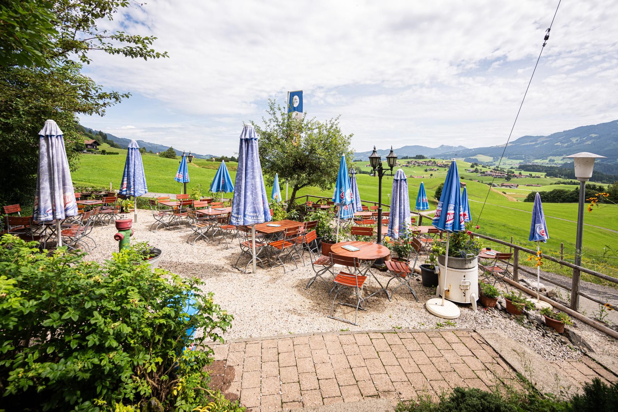 Außenbereich des Restaurants Höhlenstüble mit vielen Tischen und Stühlen. Mehrere blau-weiß gestreifte Sonnenschirme spenden Schatten.