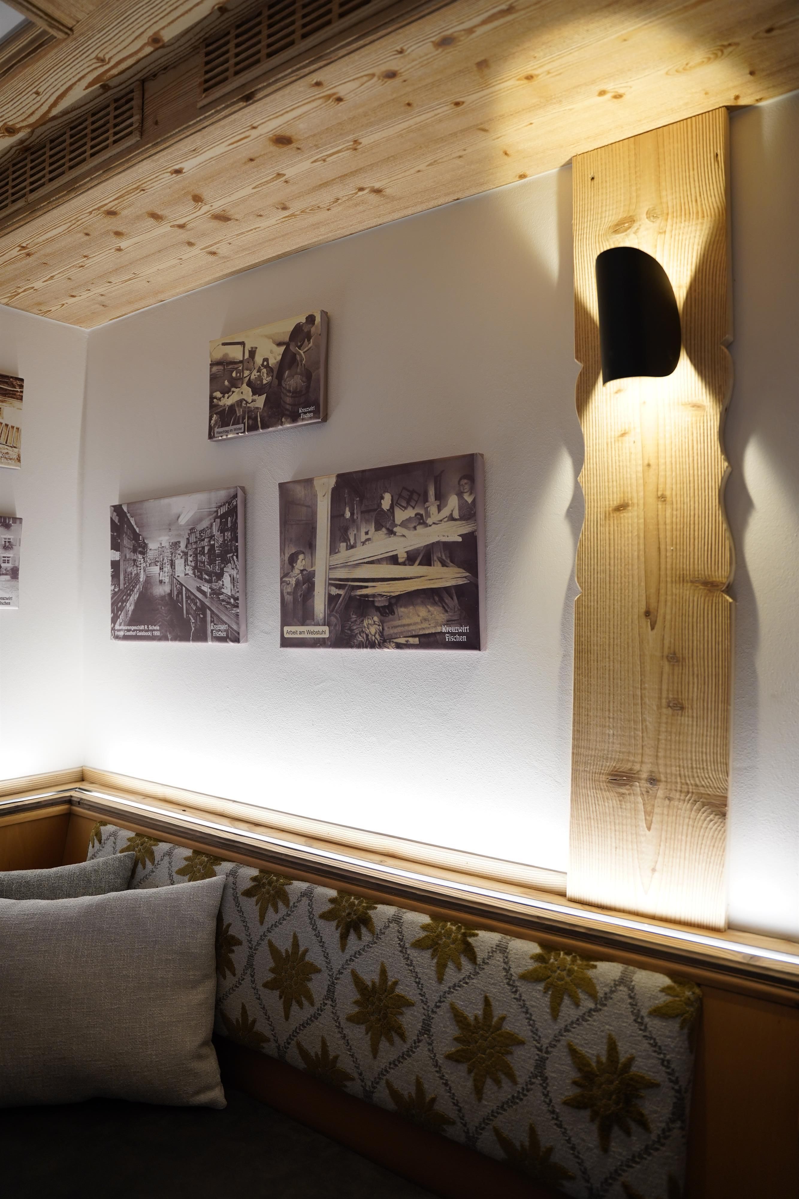 Ein gemütlicher Raum mit einer Holzdecke und Bildern an der Wand. Auf einem Holzregal steht eine kleine Lampe, die den Raum beleuchtet.