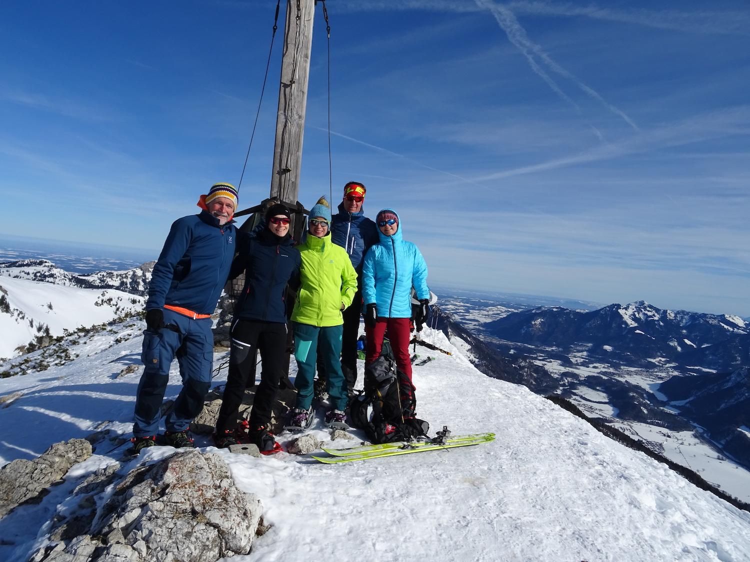 Eine Gruppe von Bergsteigern am Gipfelkreuz, es liegt noch ein wenig Schnee.
