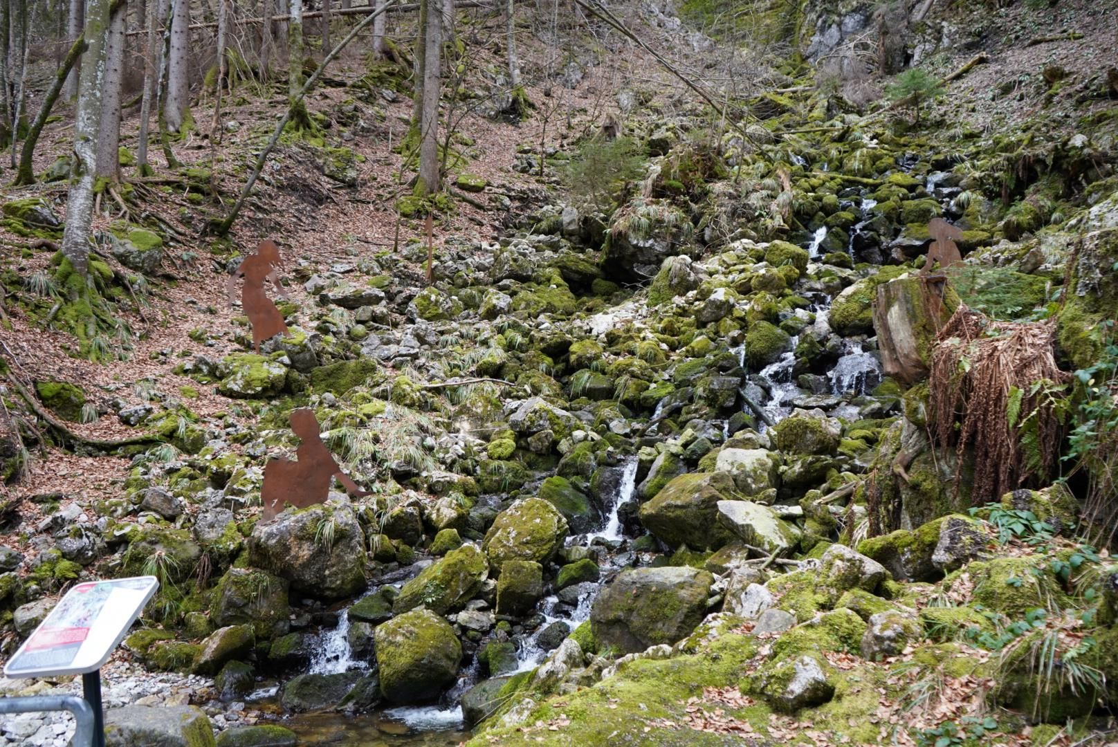 Naturbelassener Bergbach mit zahlreichen Steinen und Felsen. Das Wasser fließt über moosbewachsene Steine.