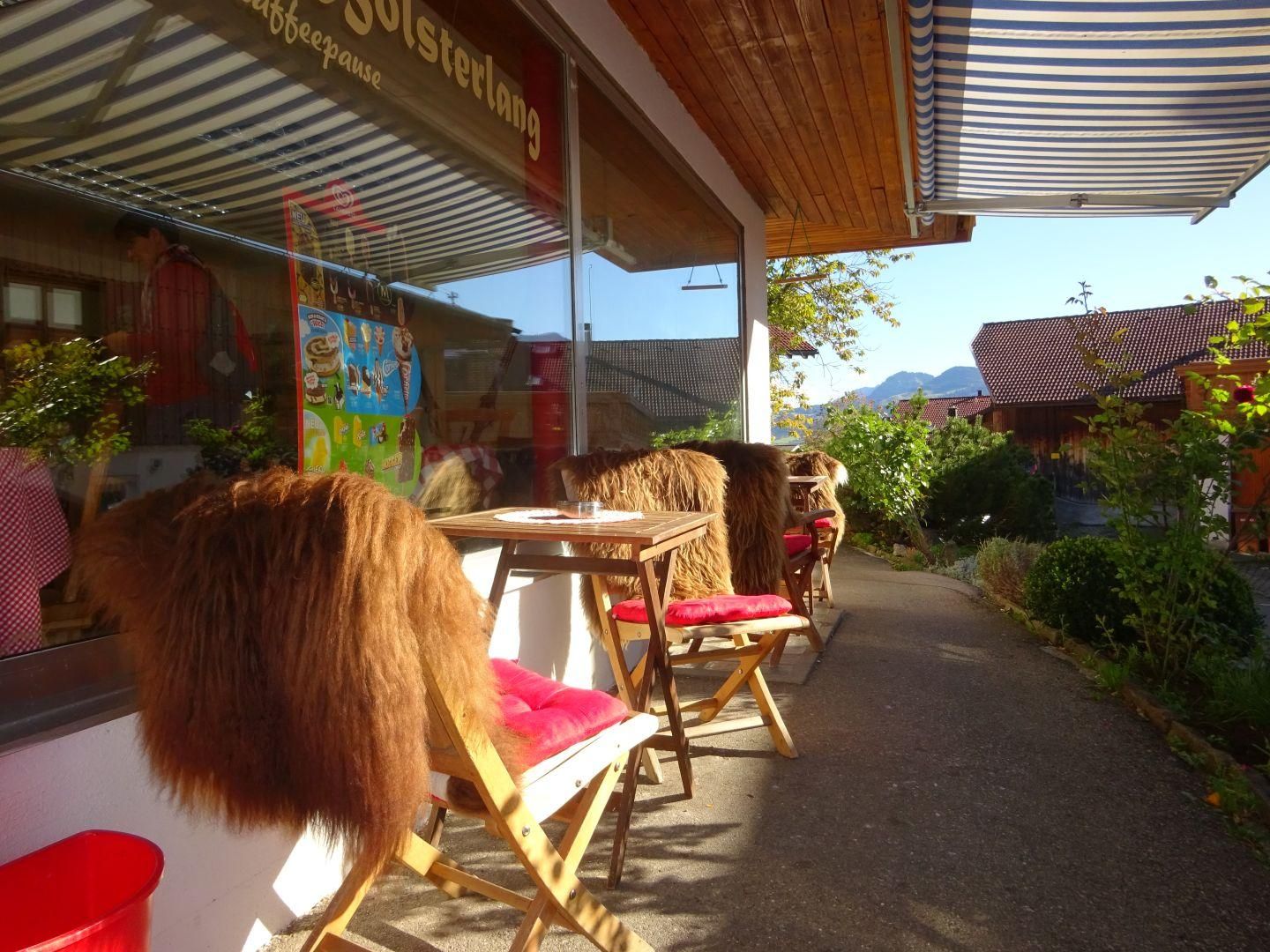 Holzstühle mit roten Kissen und braunen Fellauflagen stehen an kleinen Holztischen.
