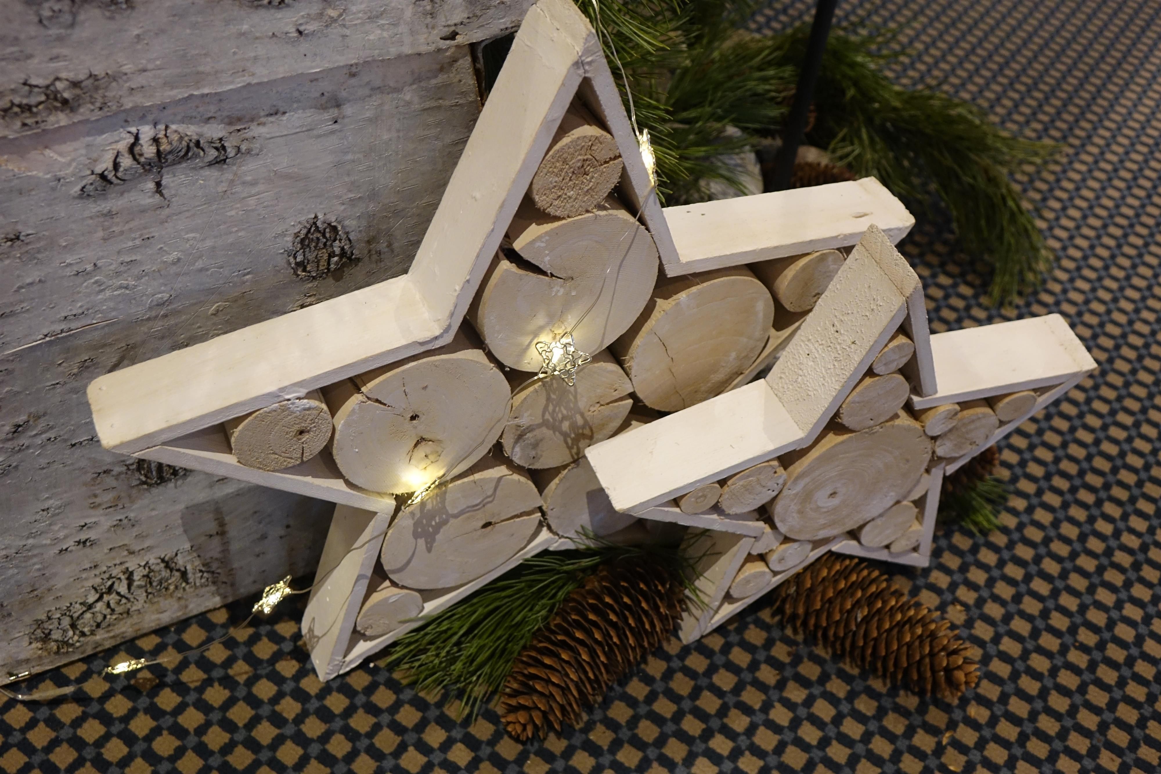 Zwei Sterne aus Holz, gefüllt mit Holzscheiben stehen als Adventsdeko vor einer Wand.