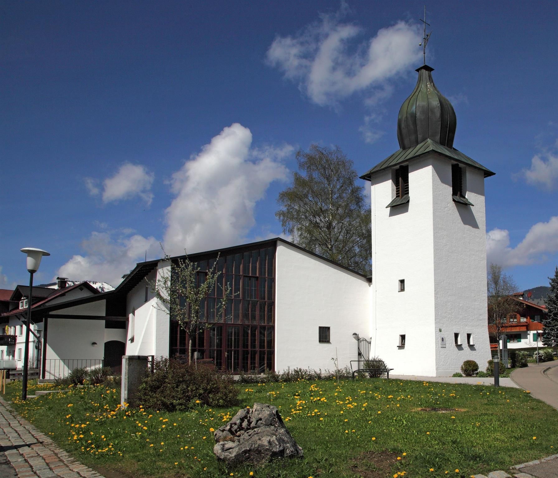 Die Evangelische Kirche "Zum Guten Hirten", rechts der Turm, im Vordergrund eine Wiese mit Löwenzahn.
