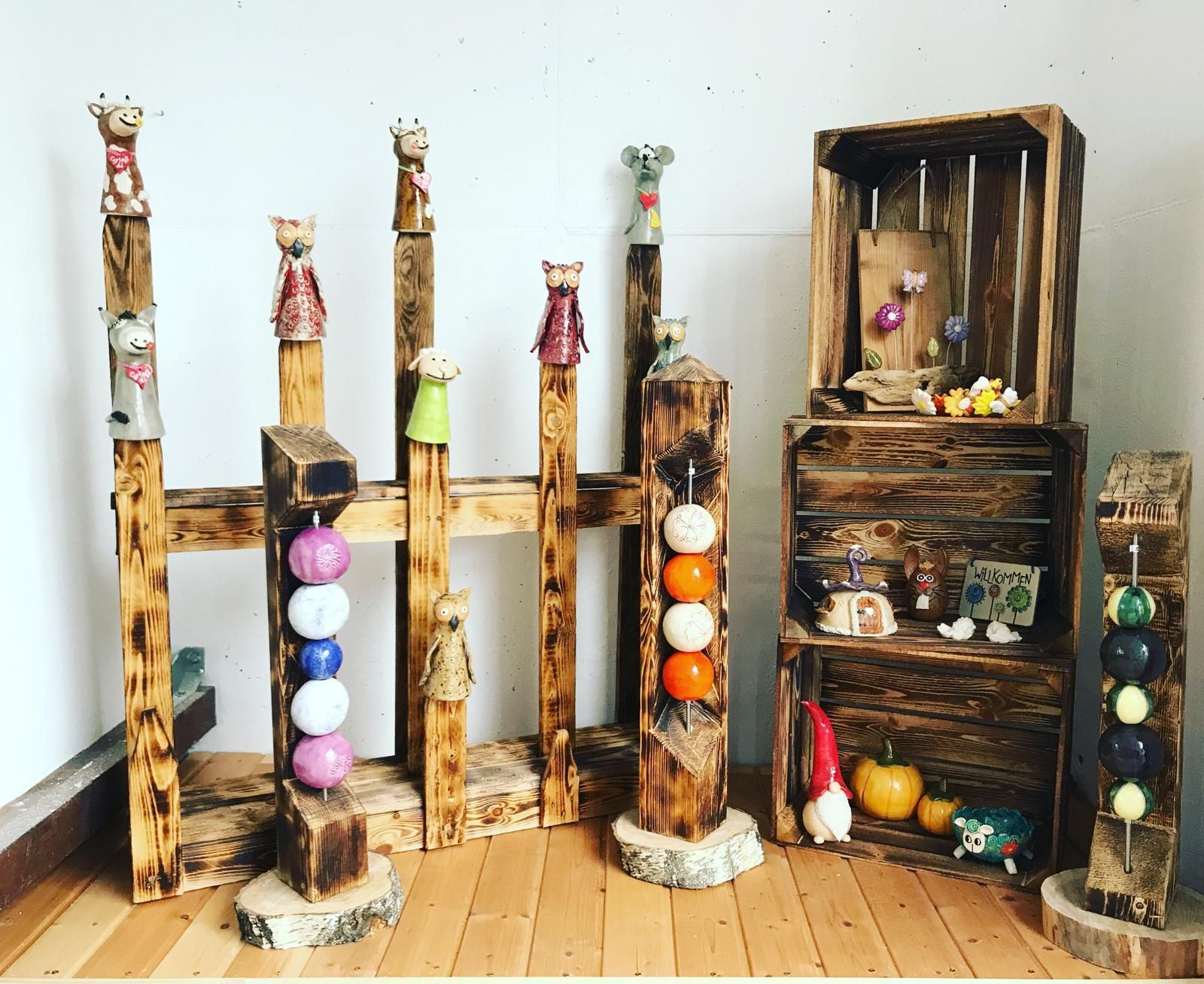 Nadjas Töpfer Krämle: Keramikfiguren auf Holzstelen, Holzkisten mit Keramikdekoration, Kürbissen und Holzschildern auf Holzboden.