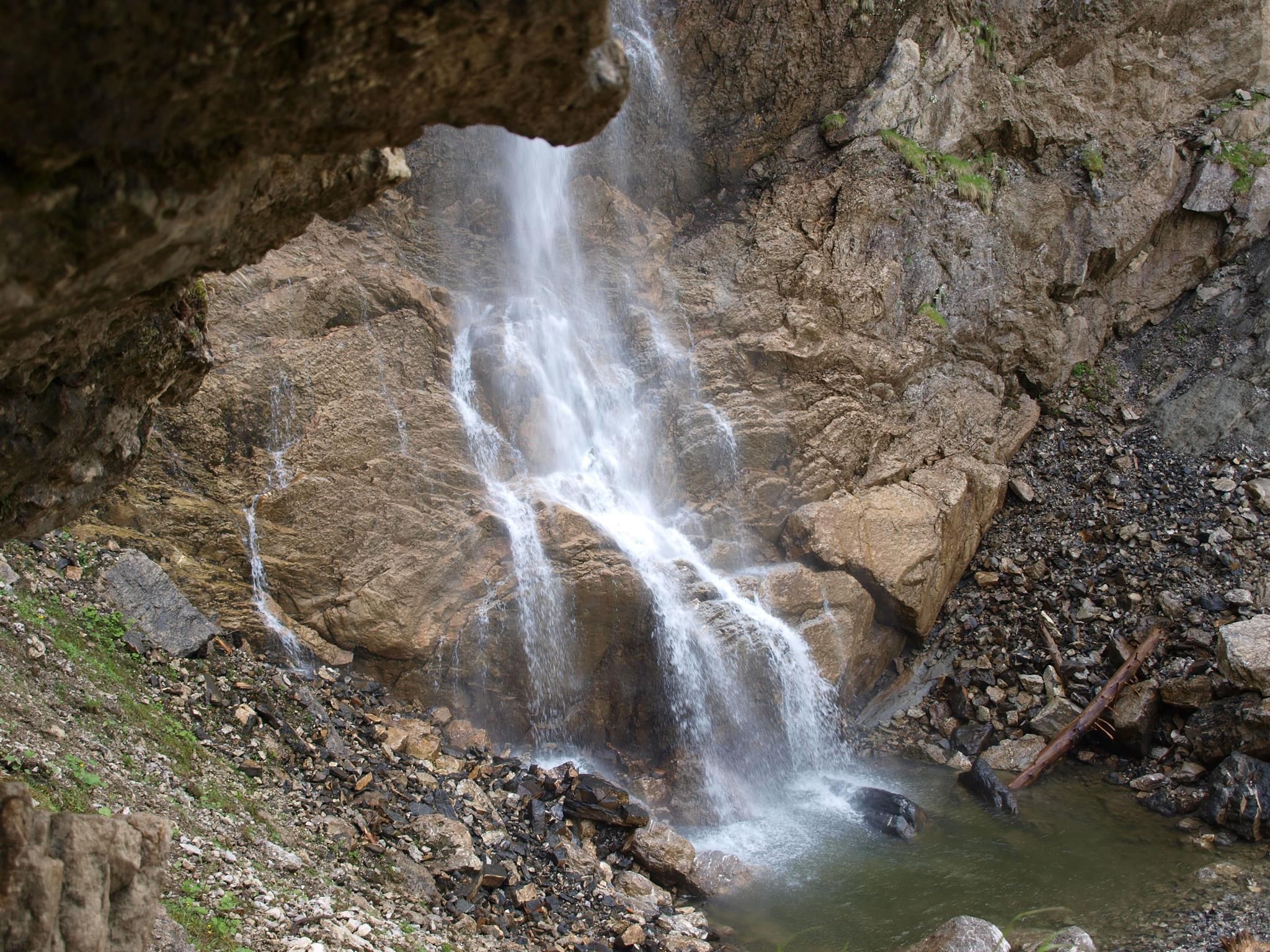 Ein mehrstufiger Wasserfall stürzt über raue, graubraune Felsen in ein kleines, dunkles Becken.
