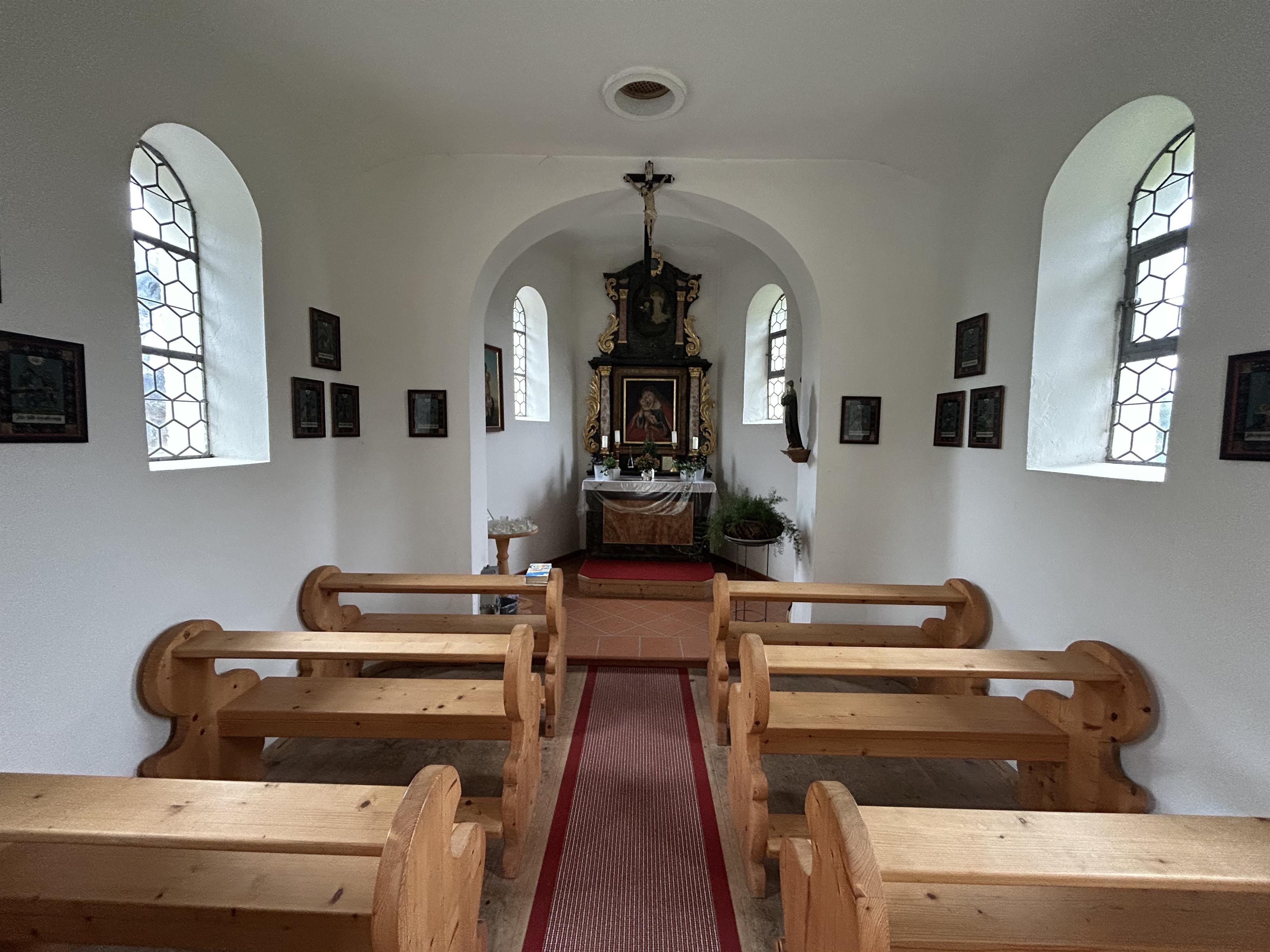 Innenansicht der Marienkapelle Dietrichs. Heller Raum mit kleinen Bildern an den Wänden. Roter Läufer auf dem Steinfußboden. Holzbänke für Besucher. Ein Rundbogen mit Kreuz an dessen Spitze führt zum Altar. Über diesem hängt ein Bild der heiligen Maria mit Kind.